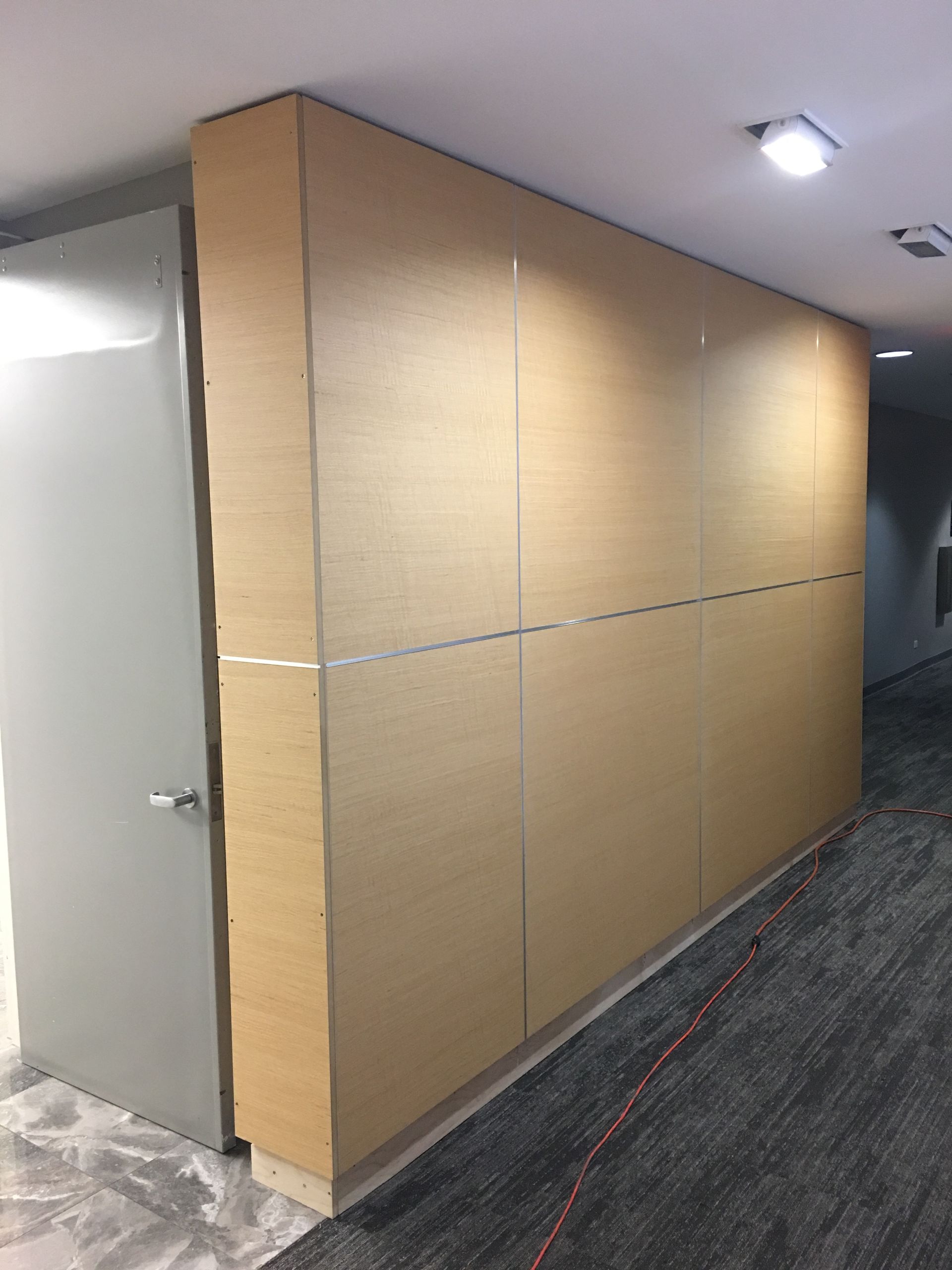 Wooden wall panels in a hallway with a gray door and carpeted floor.
