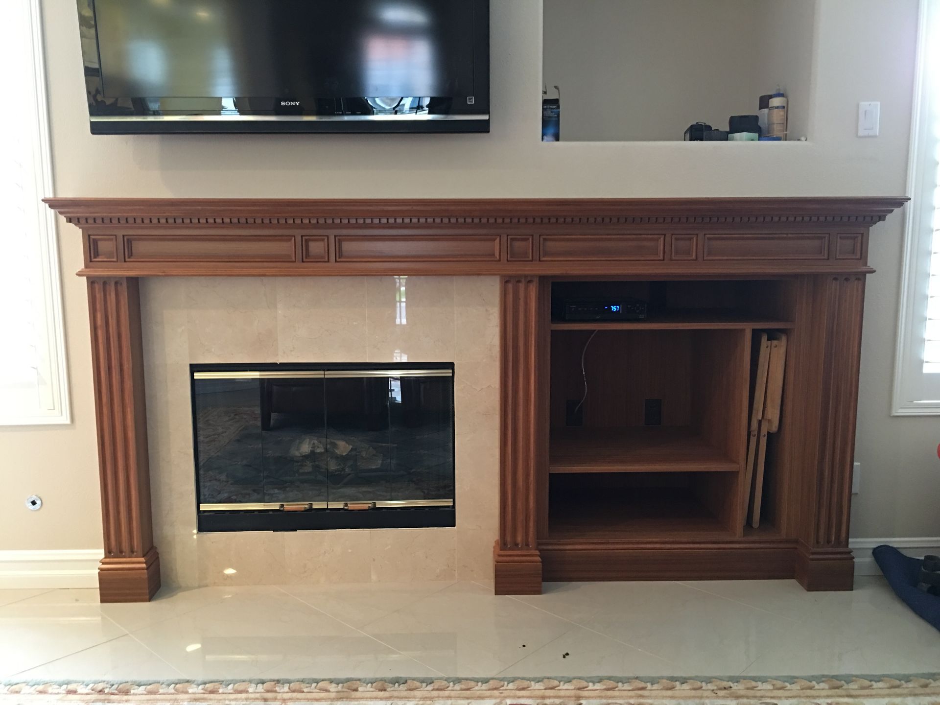 Fireplace with TV above, built-in shelves on right, all wood-toned. Beige tile and shiny floor.