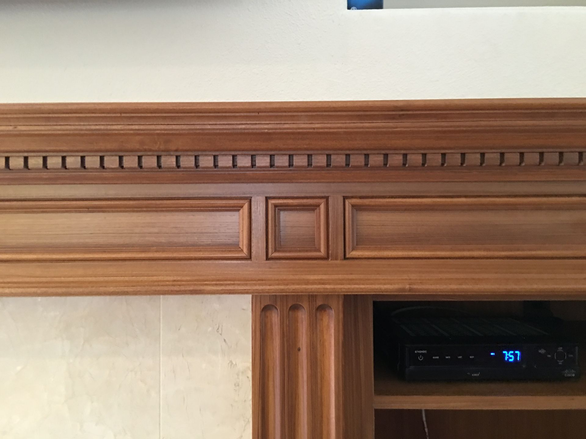 Wooden fireplace mantel with recessed panels and carved details. A media player is visible below.
