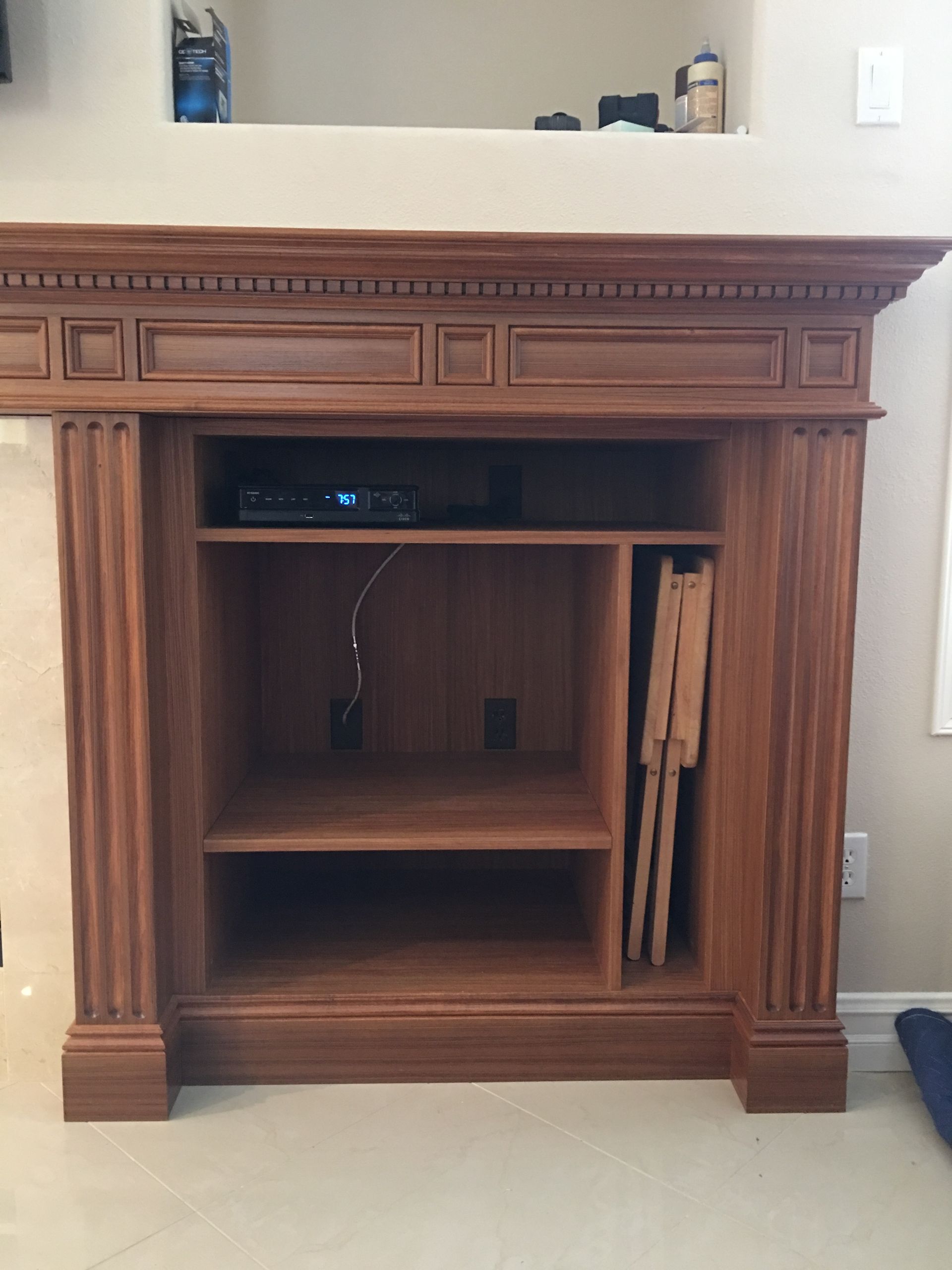 Wooden entertainment center with shelves, housing media player and folded chairs.