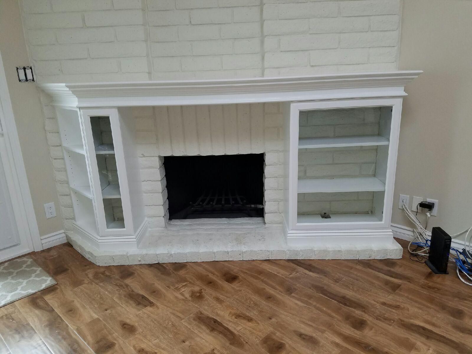 White painted brick fireplace with built-in bookshelves on either side; dark fireplace opening, wooden floor.