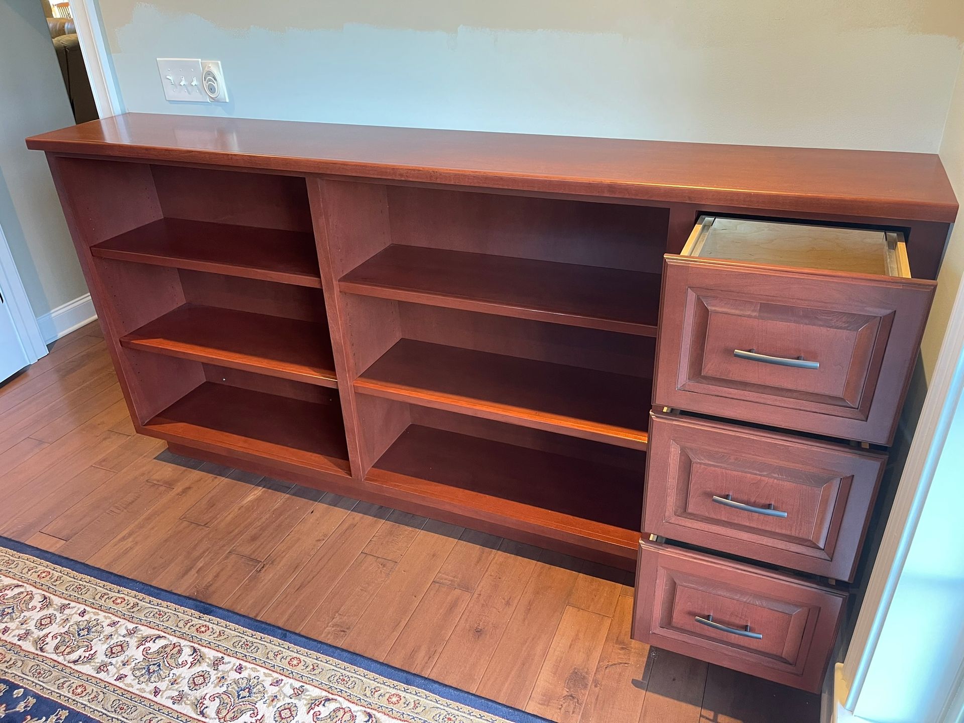 Brown wooden bookcase with shelves and drawers, set against a wall. One drawer is open.
