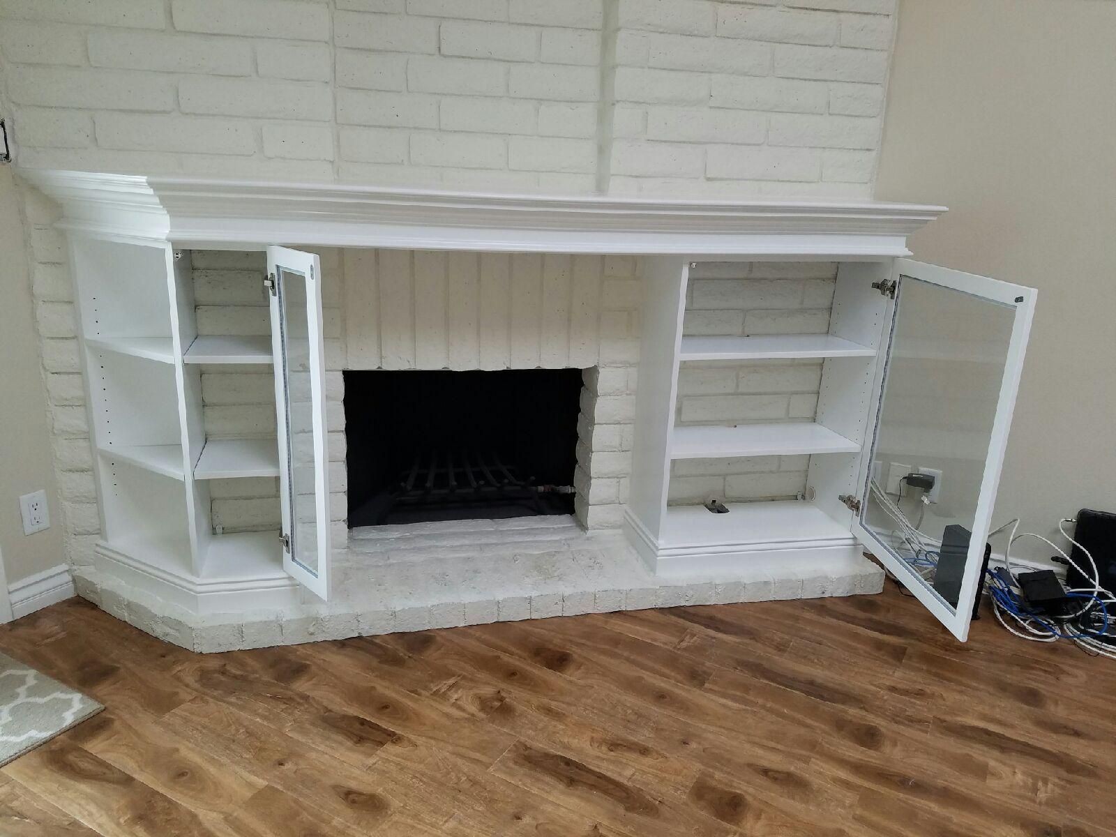White brick fireplace with built-in bookshelves. Glass door cabinets open to reveal shelves.