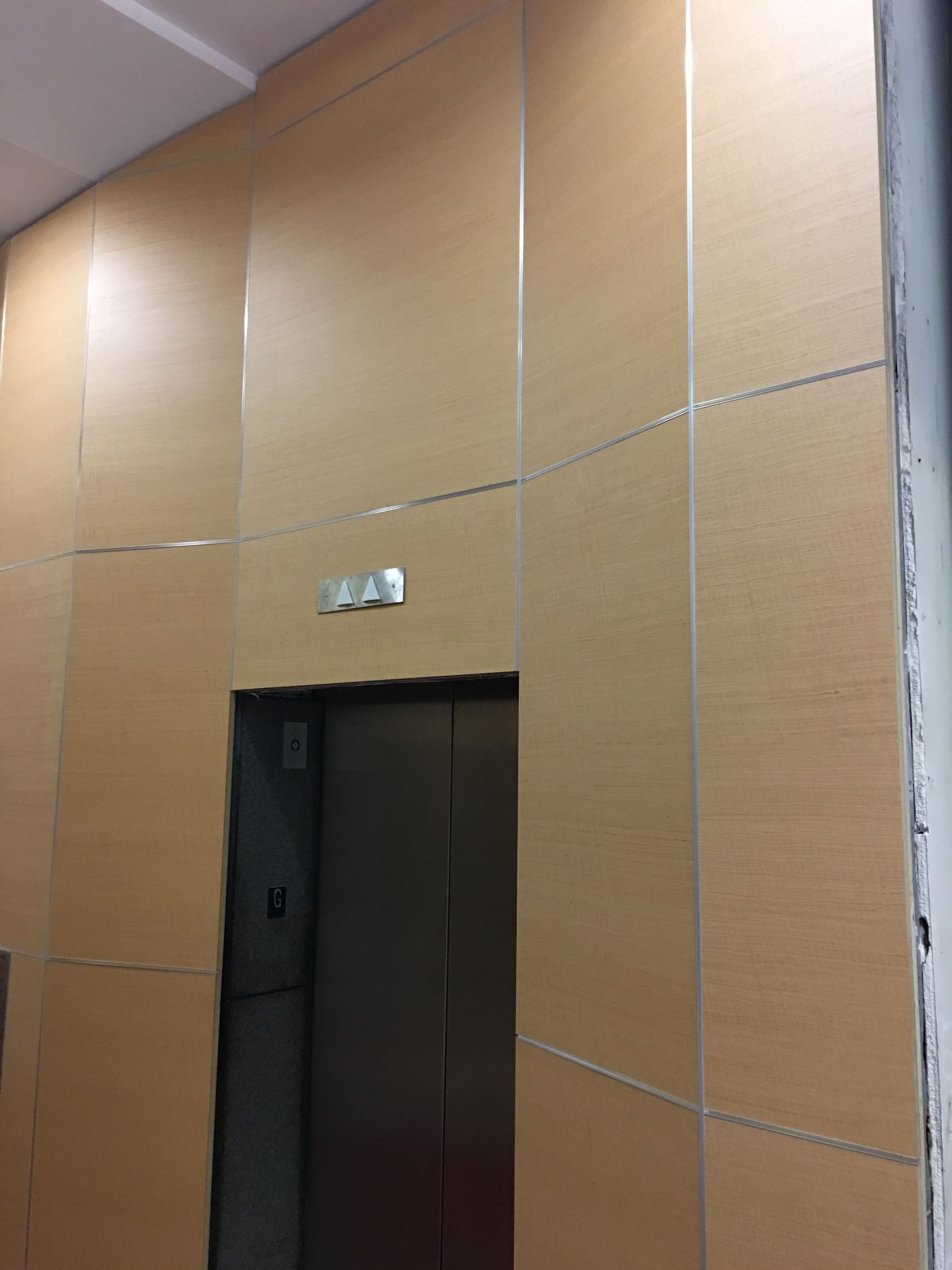 Elevator doors in a building, surrounded by light wood paneling with metal trim.