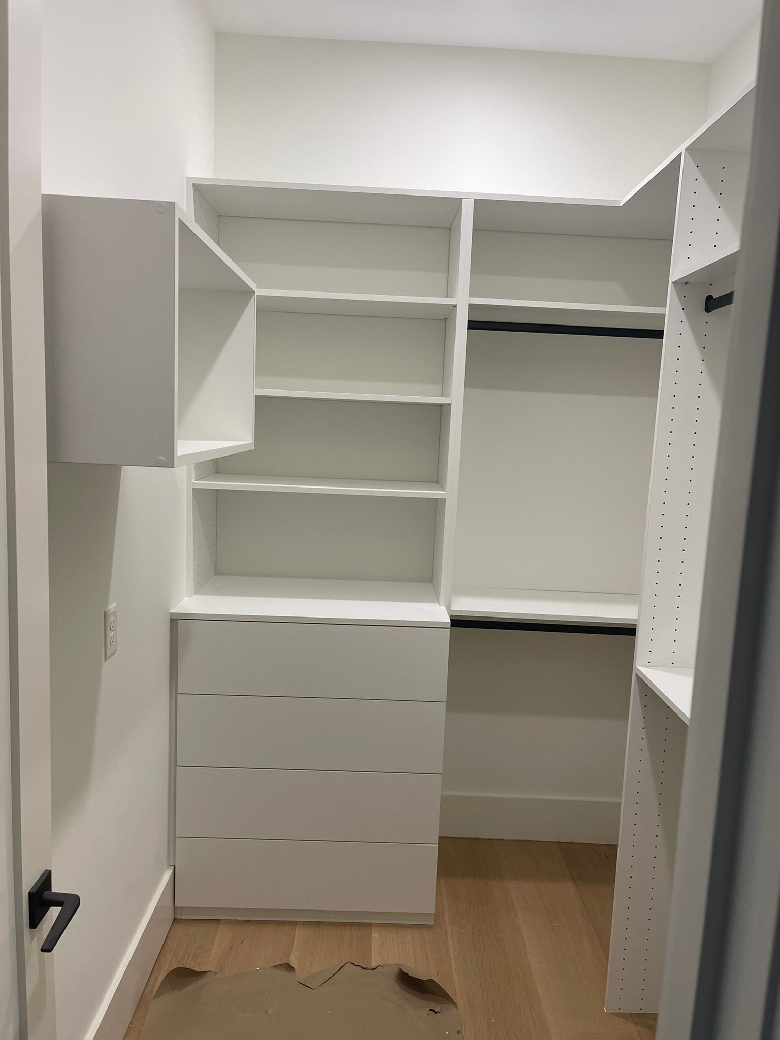 White closet with shelves, drawers, and a hanging rod, built-in against a wall with a doorway.