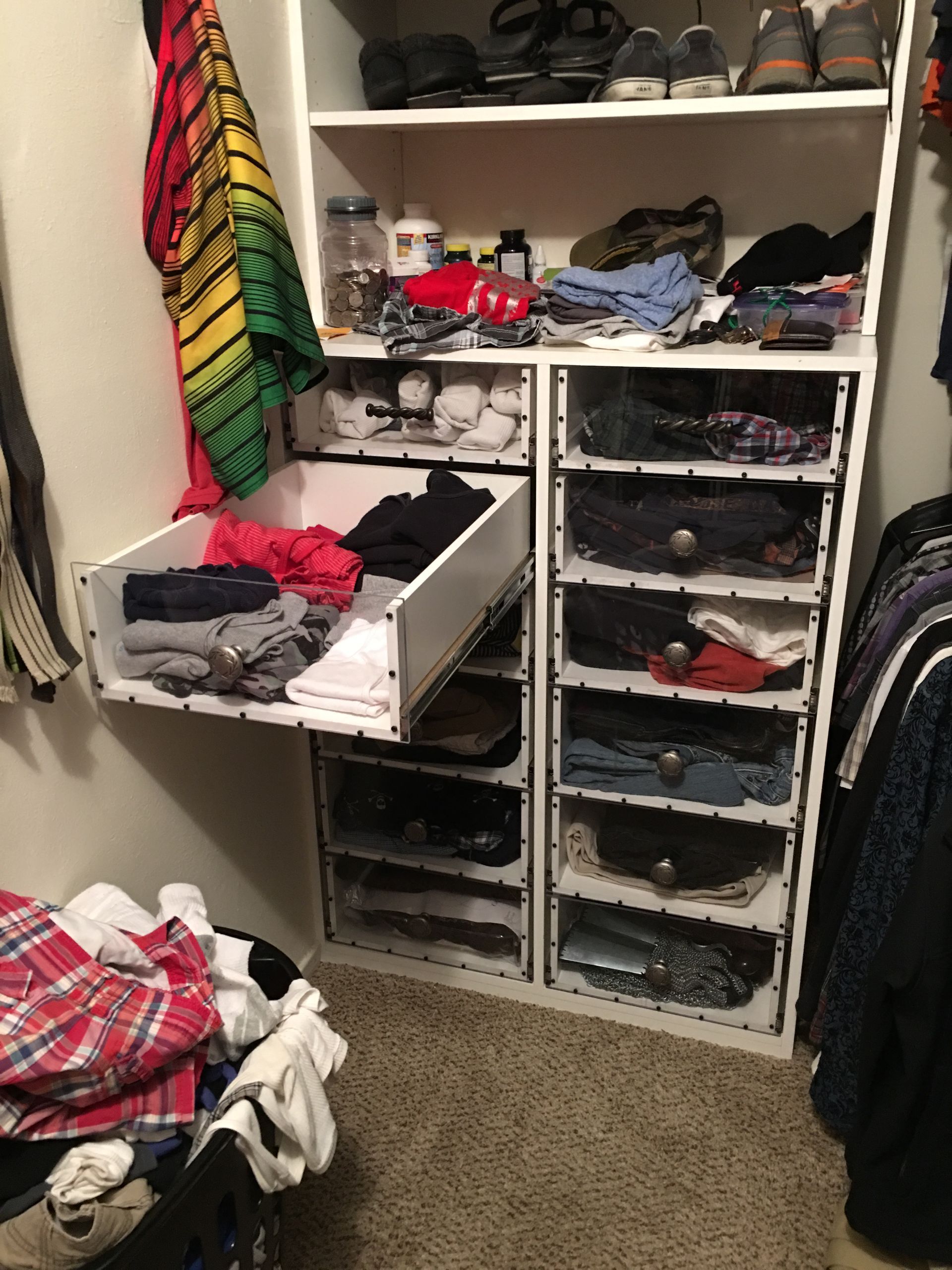 White closet with pull-out drawer open, clothes in compartments. Other clothes are nearby on the floor.