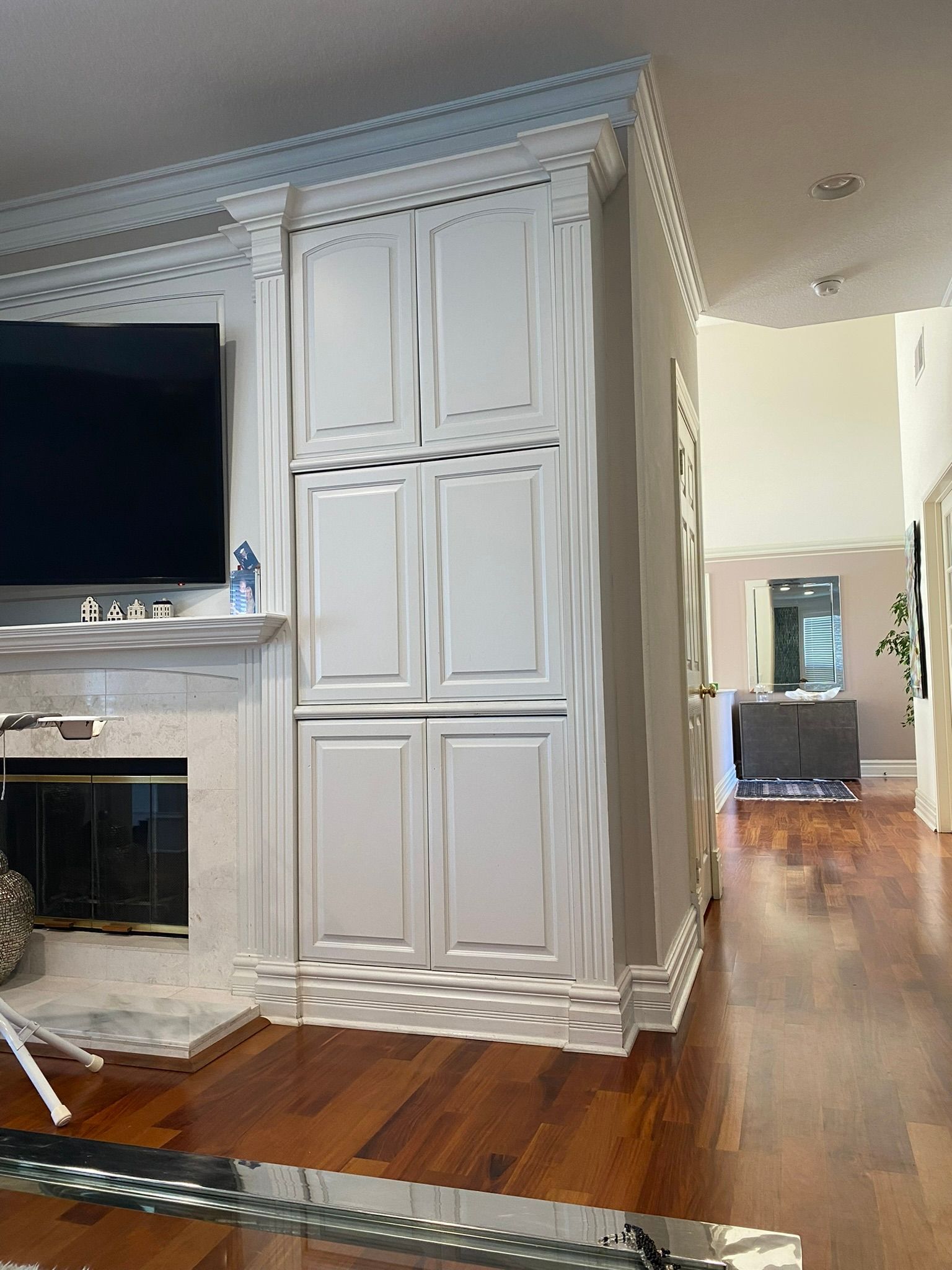 White built-in cabinets beside a fireplace. Hardwood floors, neutral walls, and a hallway are visible.
