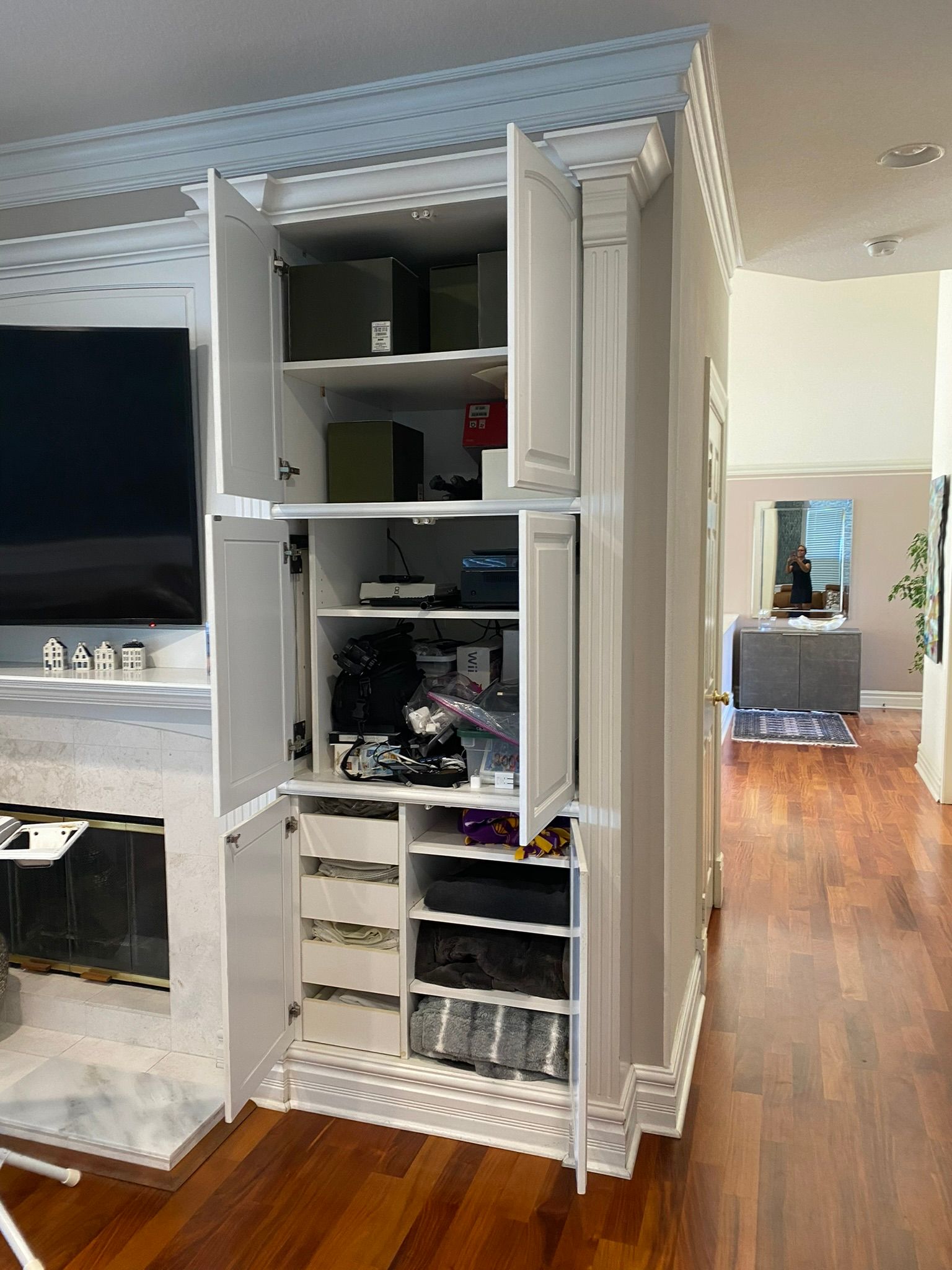 White built-in cabinet with open doors, housing electronics and shelves. Interior with black components, wood floor visible.