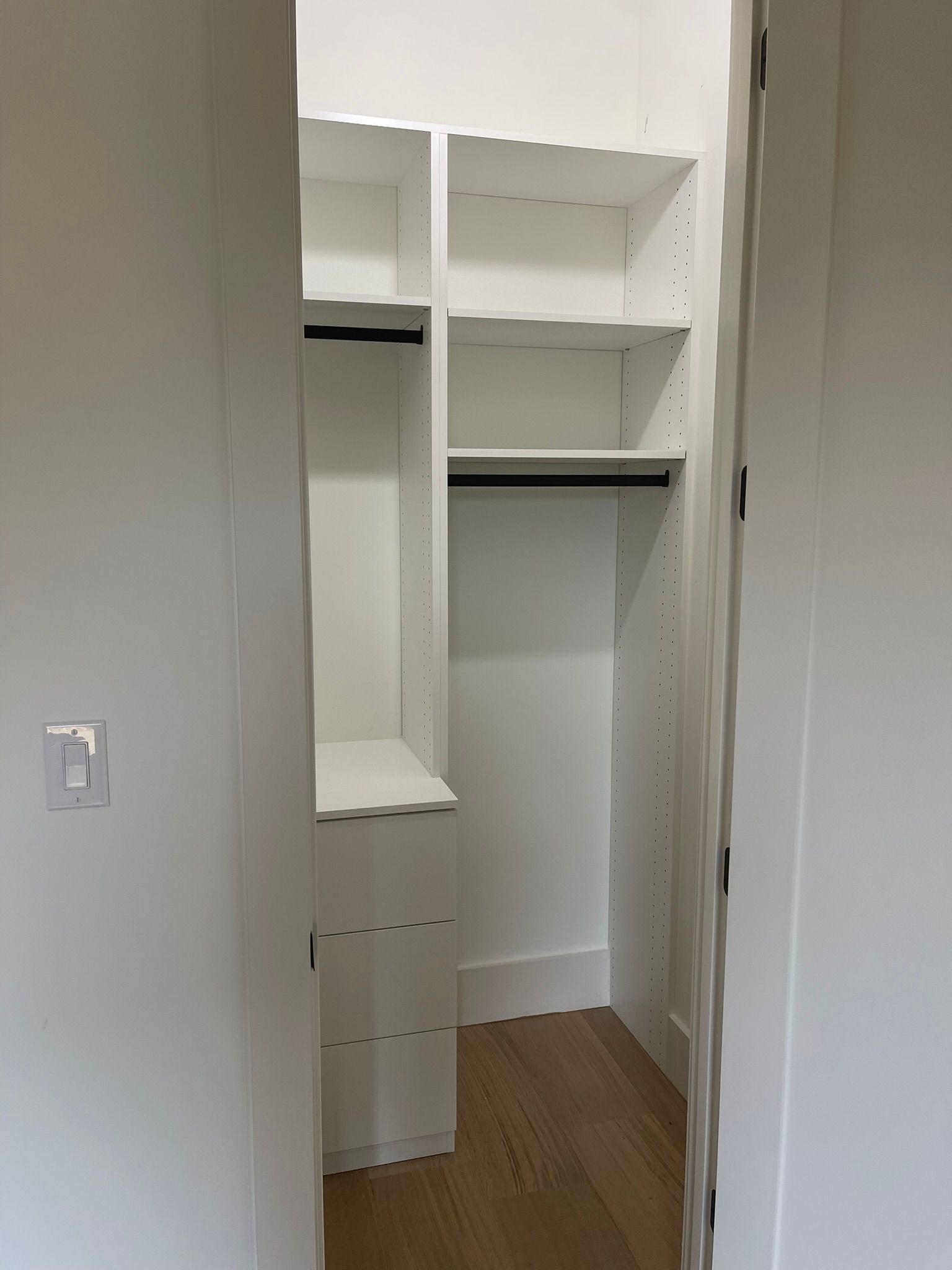 Empty, white closet with built-in shelves and a hanging rod. Light oak flooring.