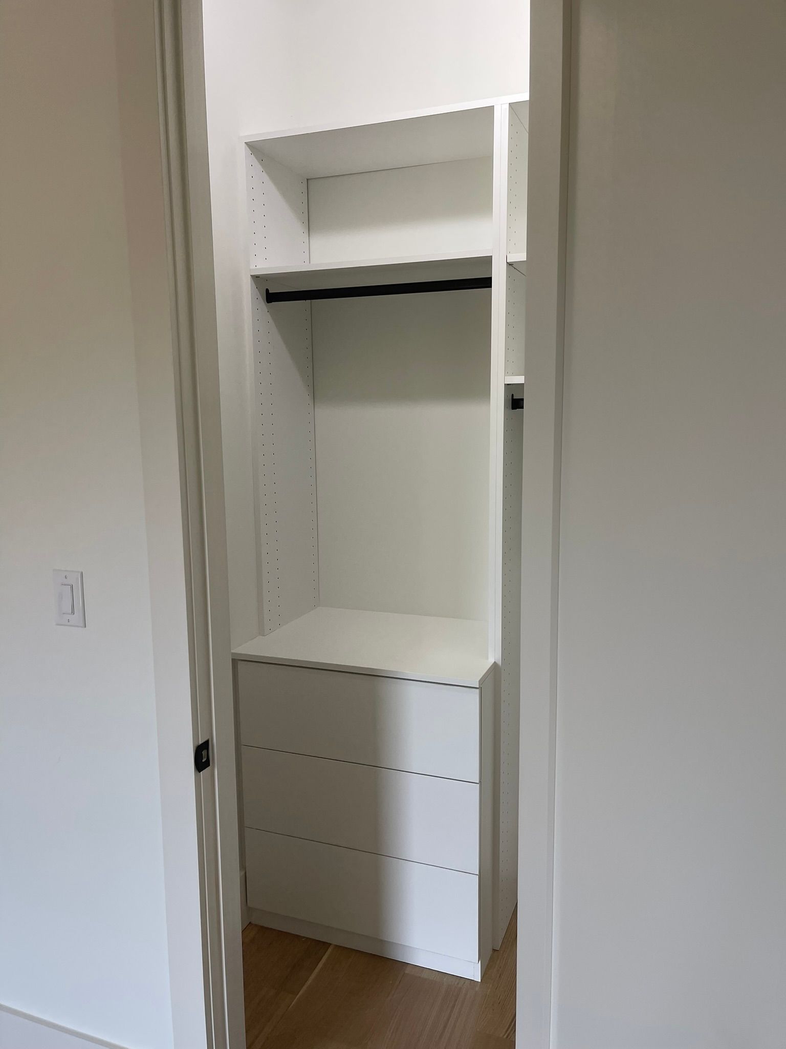 White closet interior with shelves, drawers, and a hanging rod.