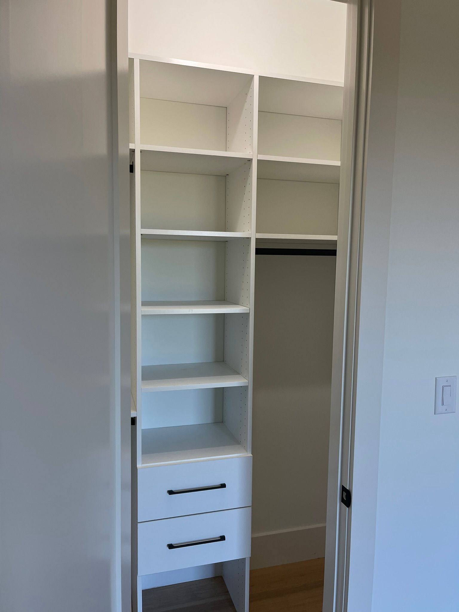White closet interior with shelves, drawers, and hanging rod.