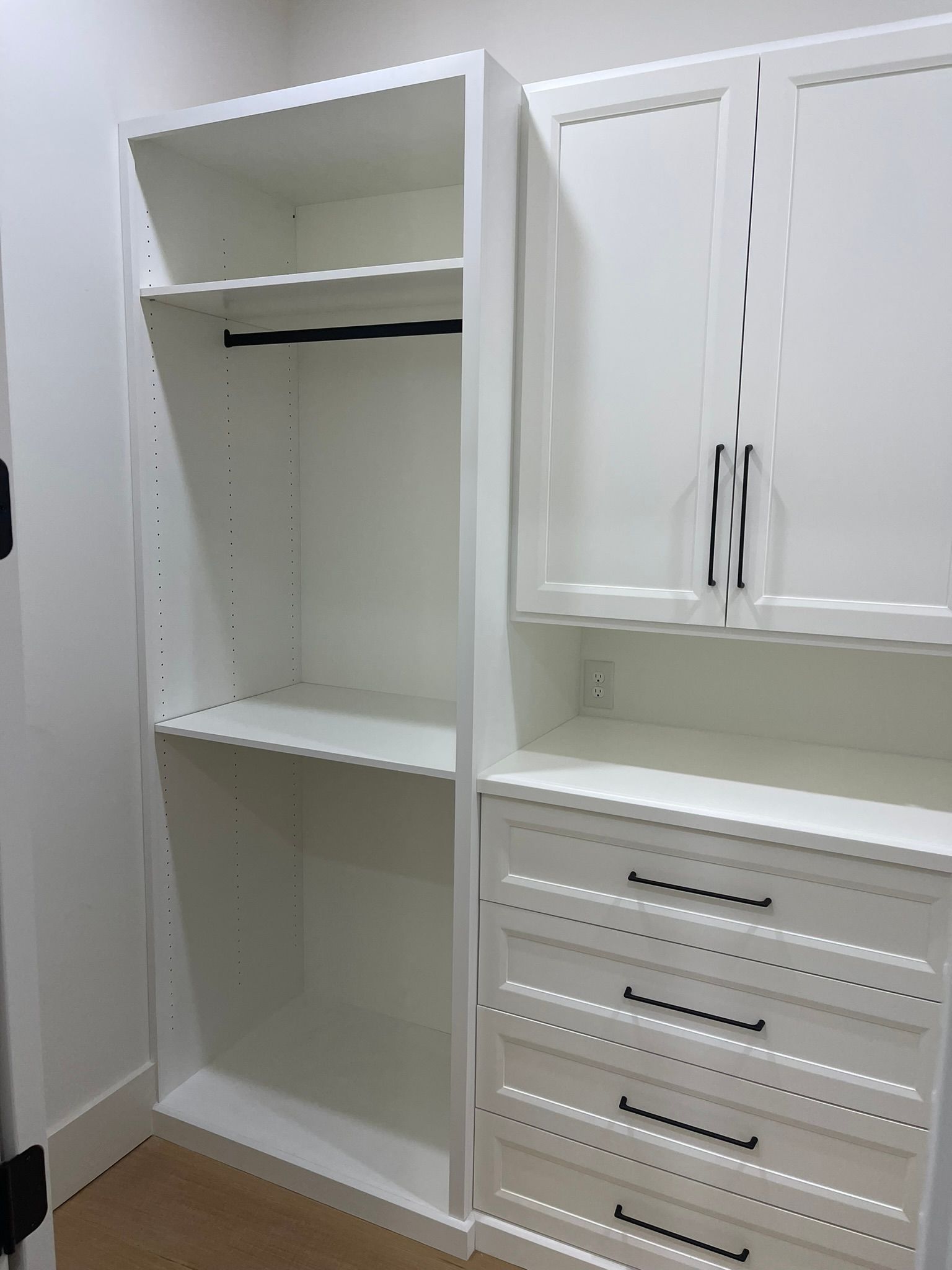 White closet organizer with hanging rod, shelves, drawers, and cabinet doors; black hardware.