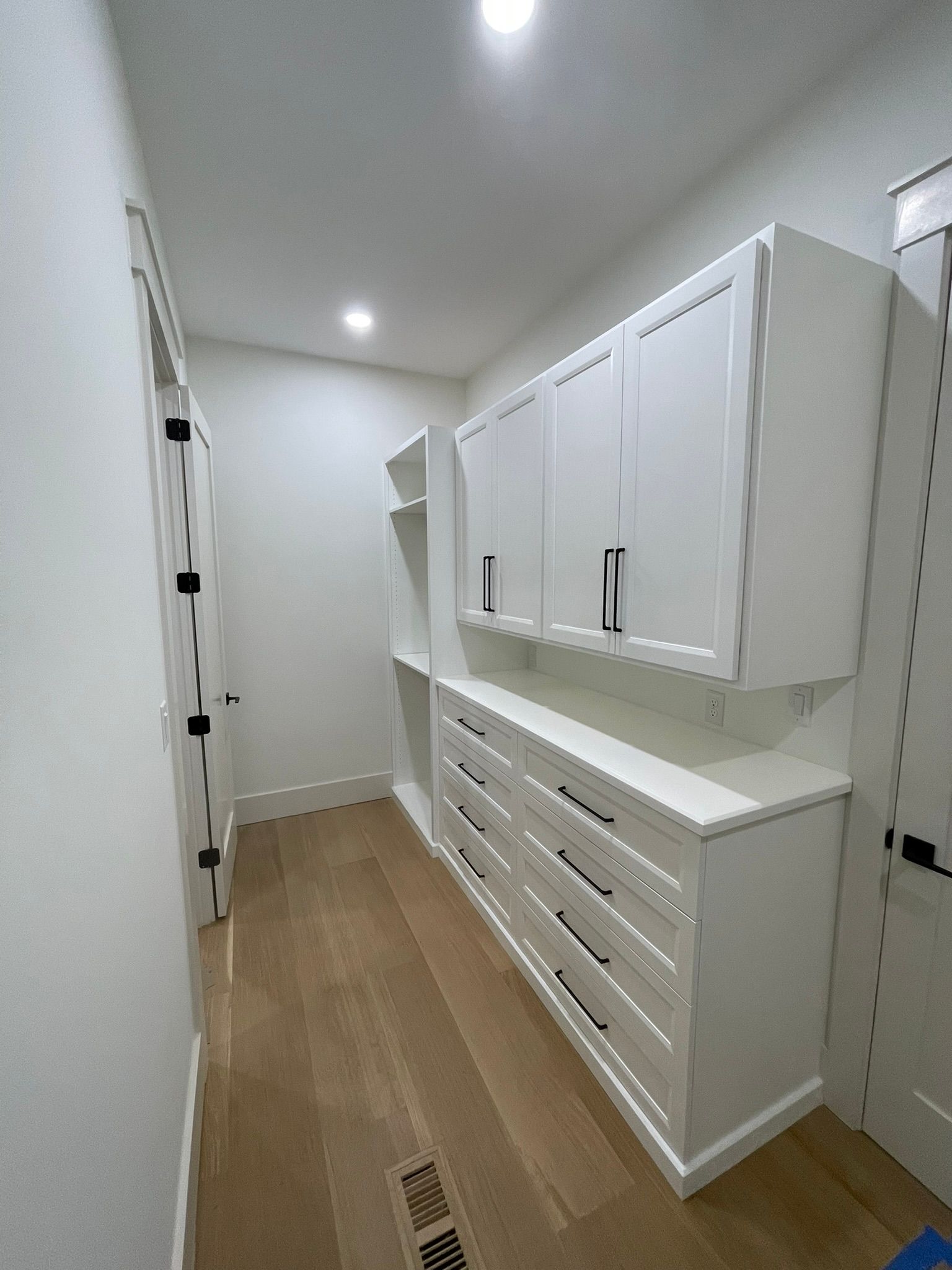 White walk-in closet with cabinets and drawers, light wood floor, and a door on the left side.