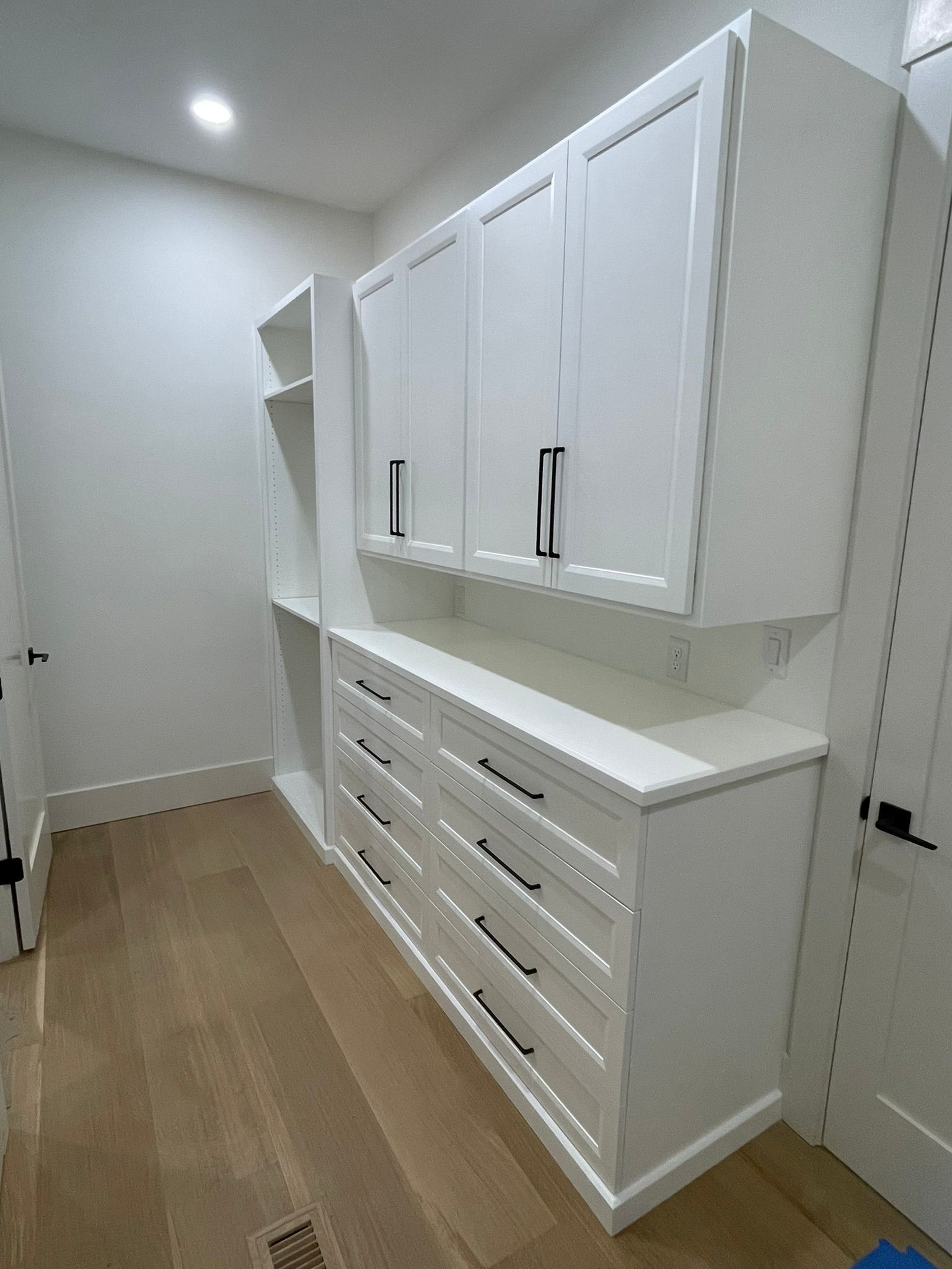 White built-in storage cabinets with drawers and overhead cupboards in a room with hardwood floors.