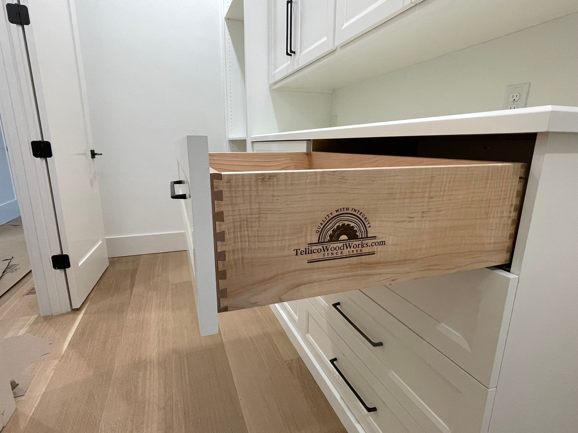 White cabinet with an open wooden drawer, hardwood floors, and a door in the background.