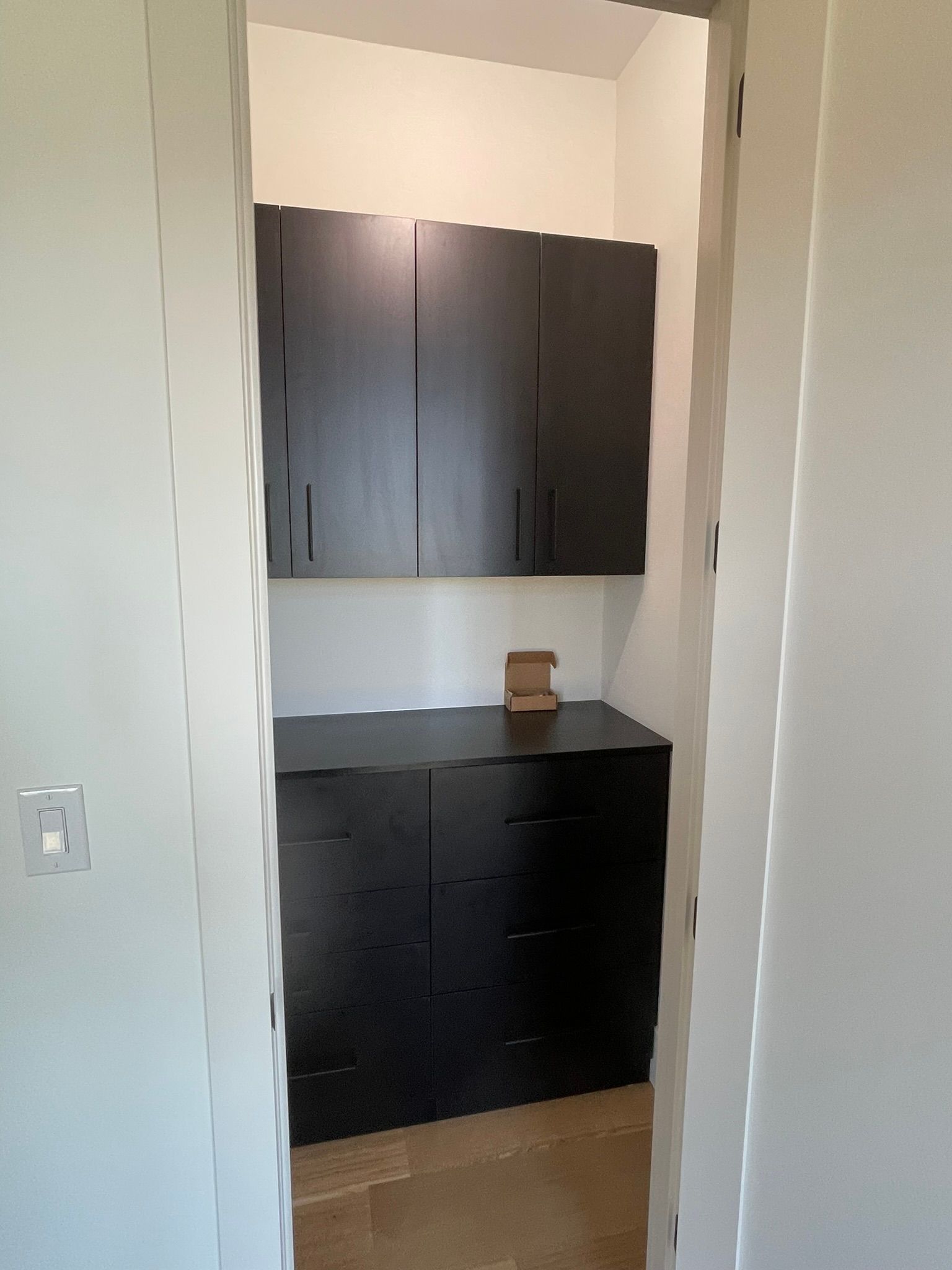 Dark cabinets in a narrow entryway. A light switch is on the left wall.