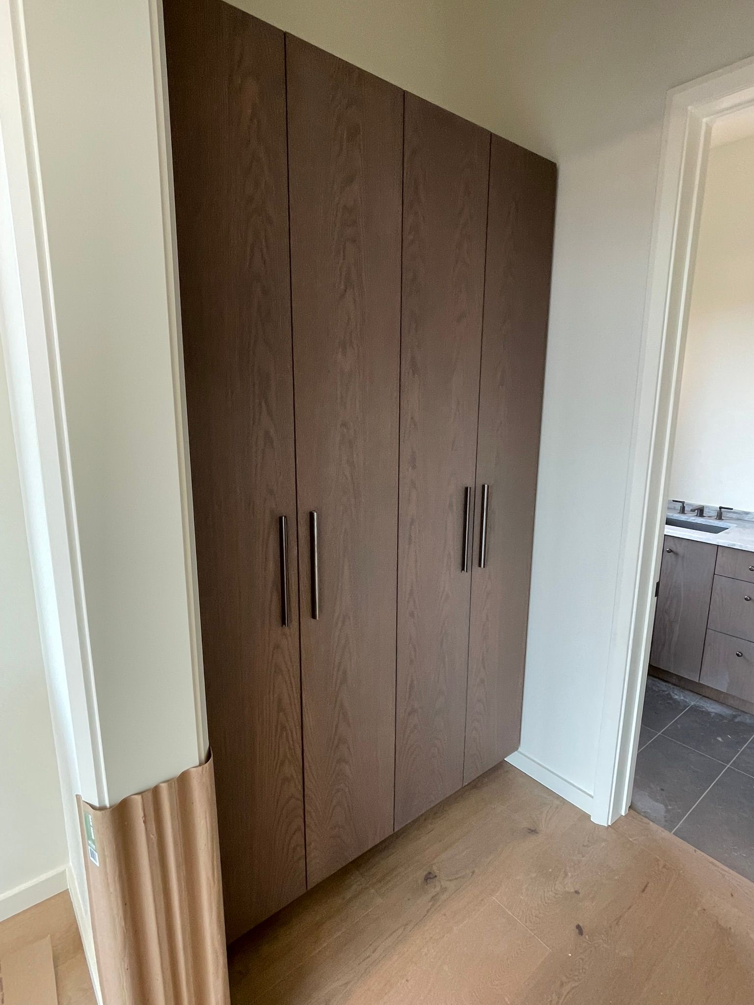 A built-in brown wood grain closet with dark handles in a hallway.
