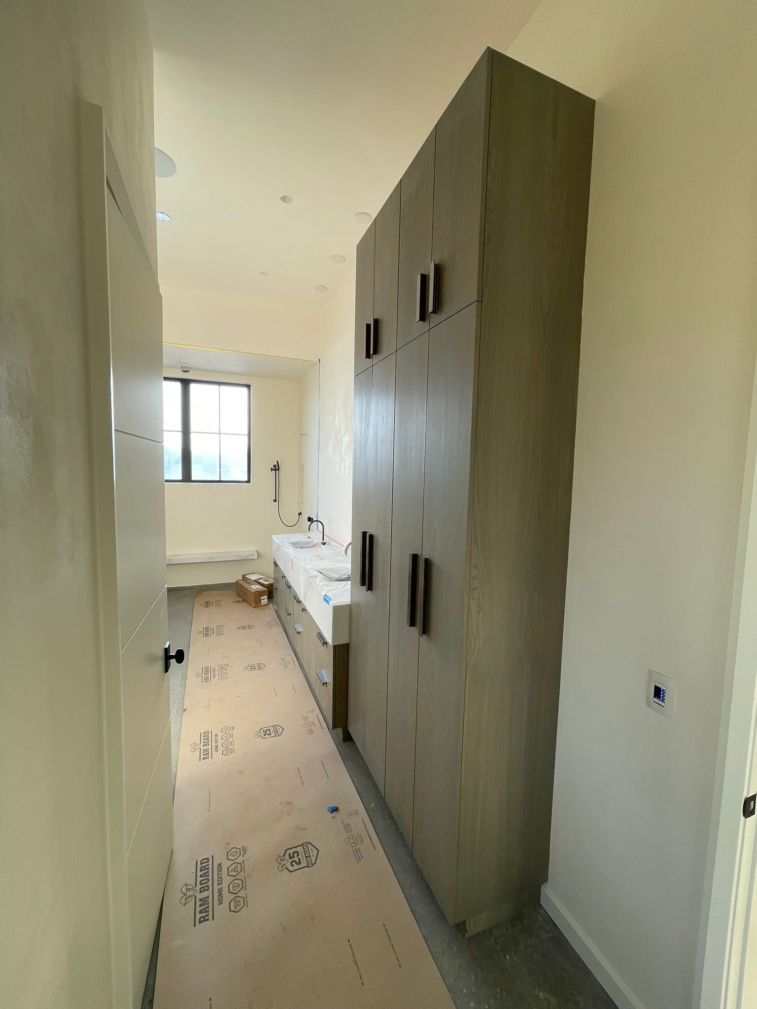 Bathroom with tall wooden cabinet, white counter, window, and open doorway.