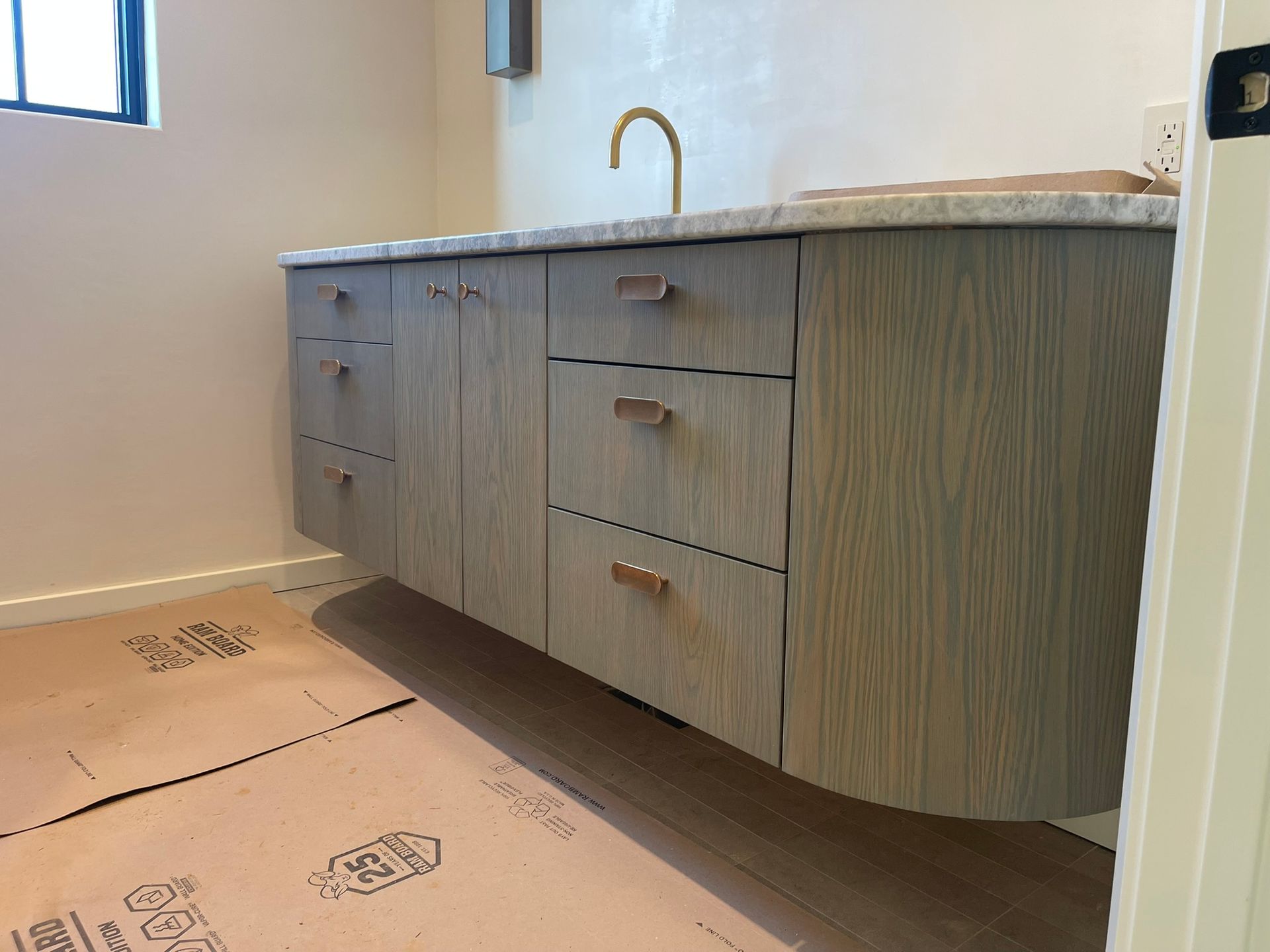 Floating wooden bathroom vanity with marble countertop and gold faucet.