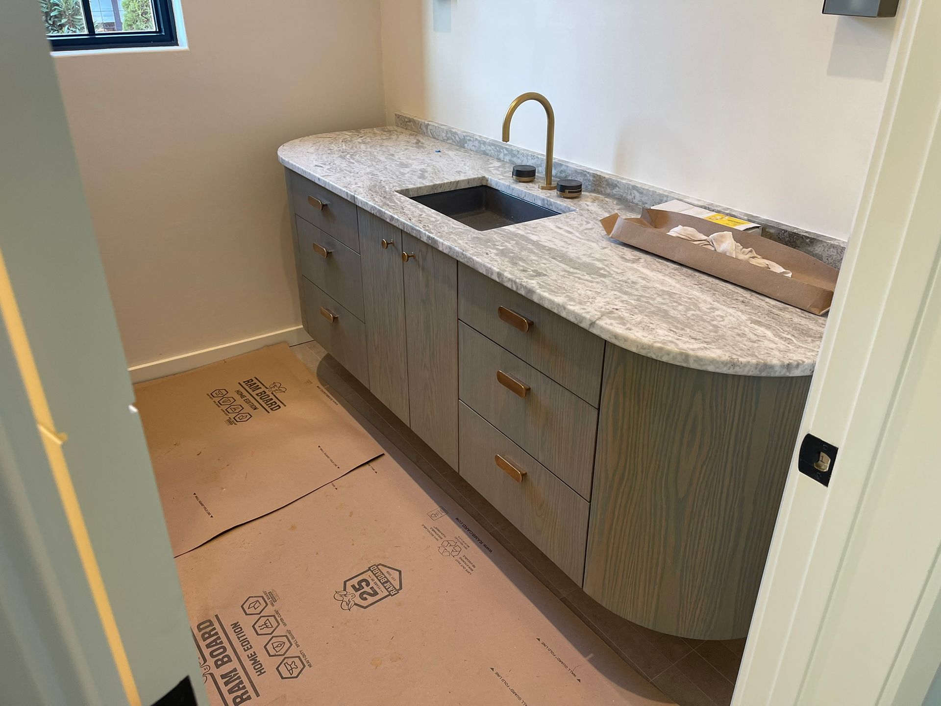 Light wood vanity with stone countertop and gold faucet in a small room.