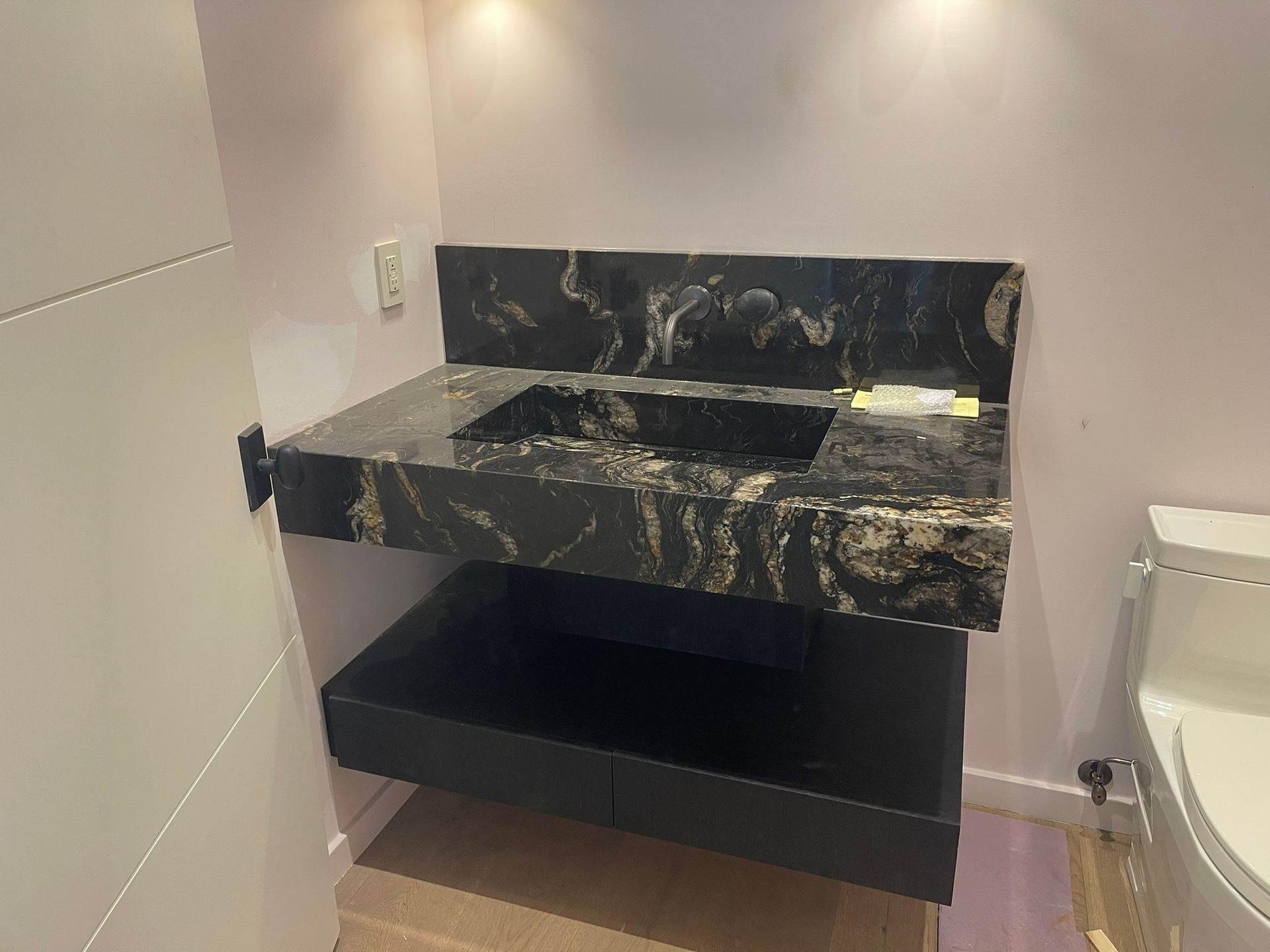 Black granite floating vanity with a built-in sink and a black storage drawer in a bathroom.