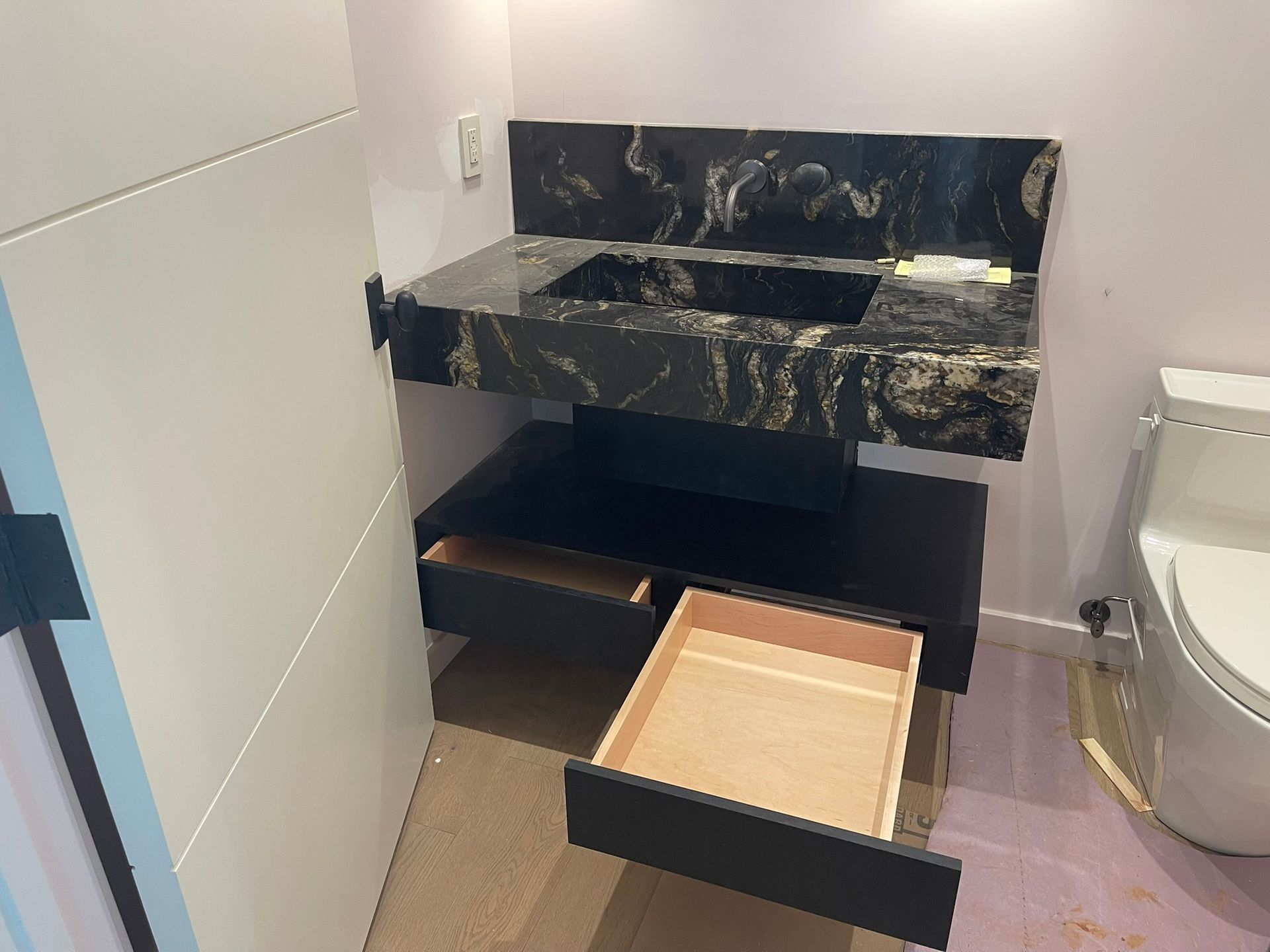 Modern black vanity with two drawers and black marble countertop in a bathroom.