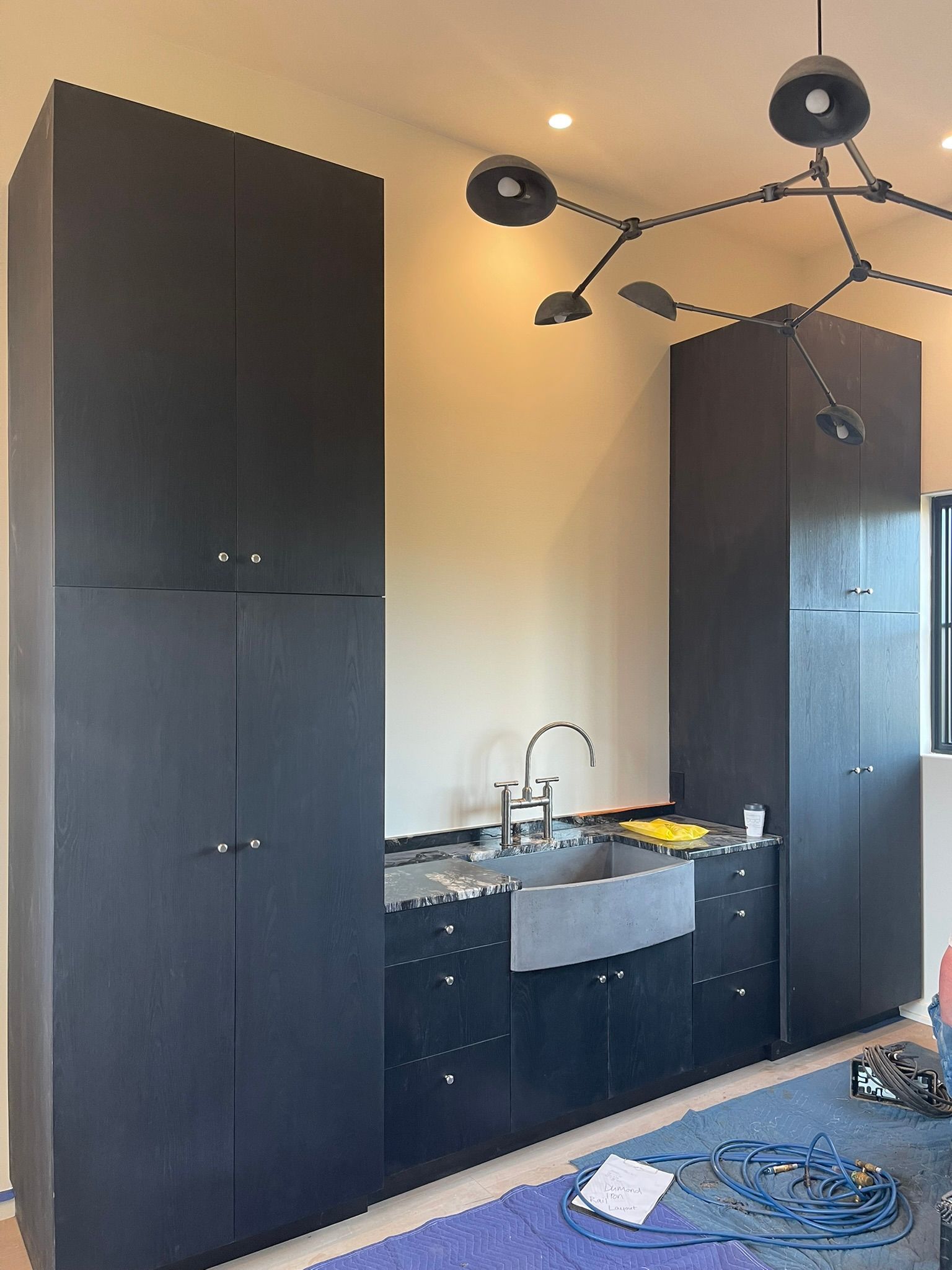 Dark gray cabinetry with sink, set against beige walls. Modern light fixture above.