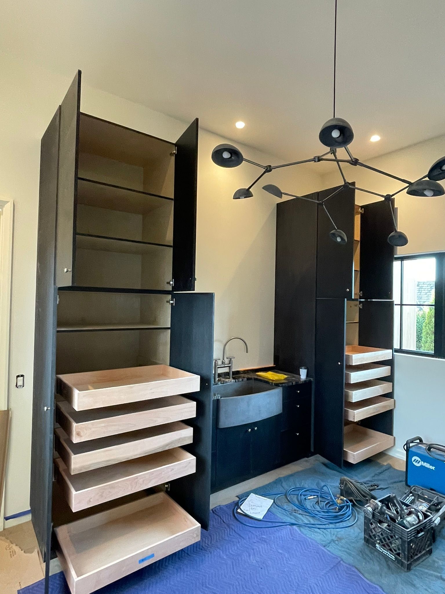 Kitchen cabinets under construction with open shelves and drawers; a sink and a modern light fixture.