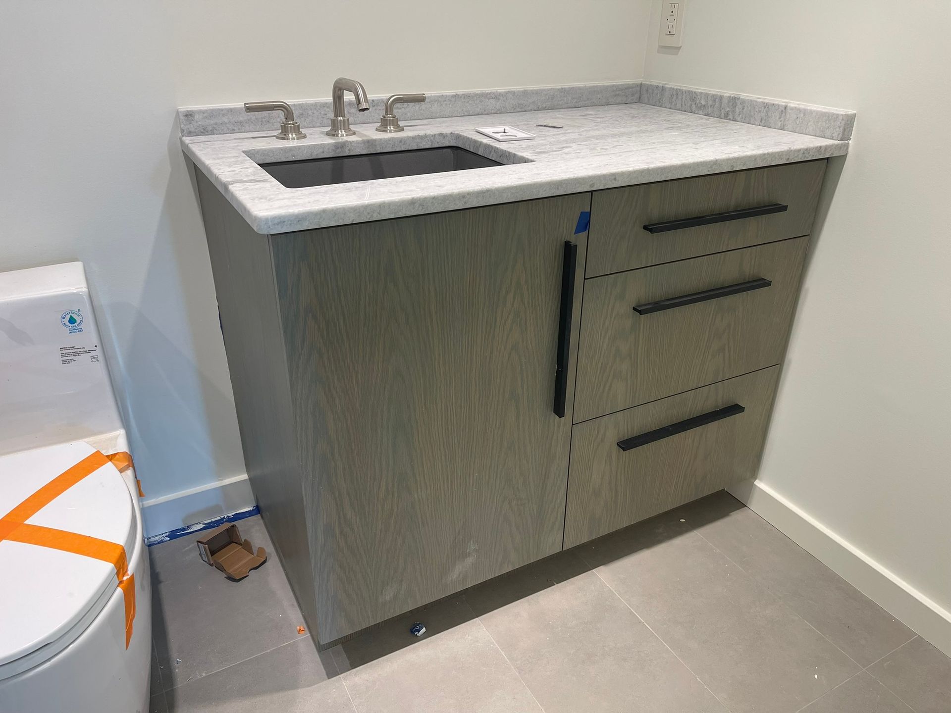 Bathroom vanity with gray cabinet, marble countertop, and rectangular sink. Three drawers and a faucet.