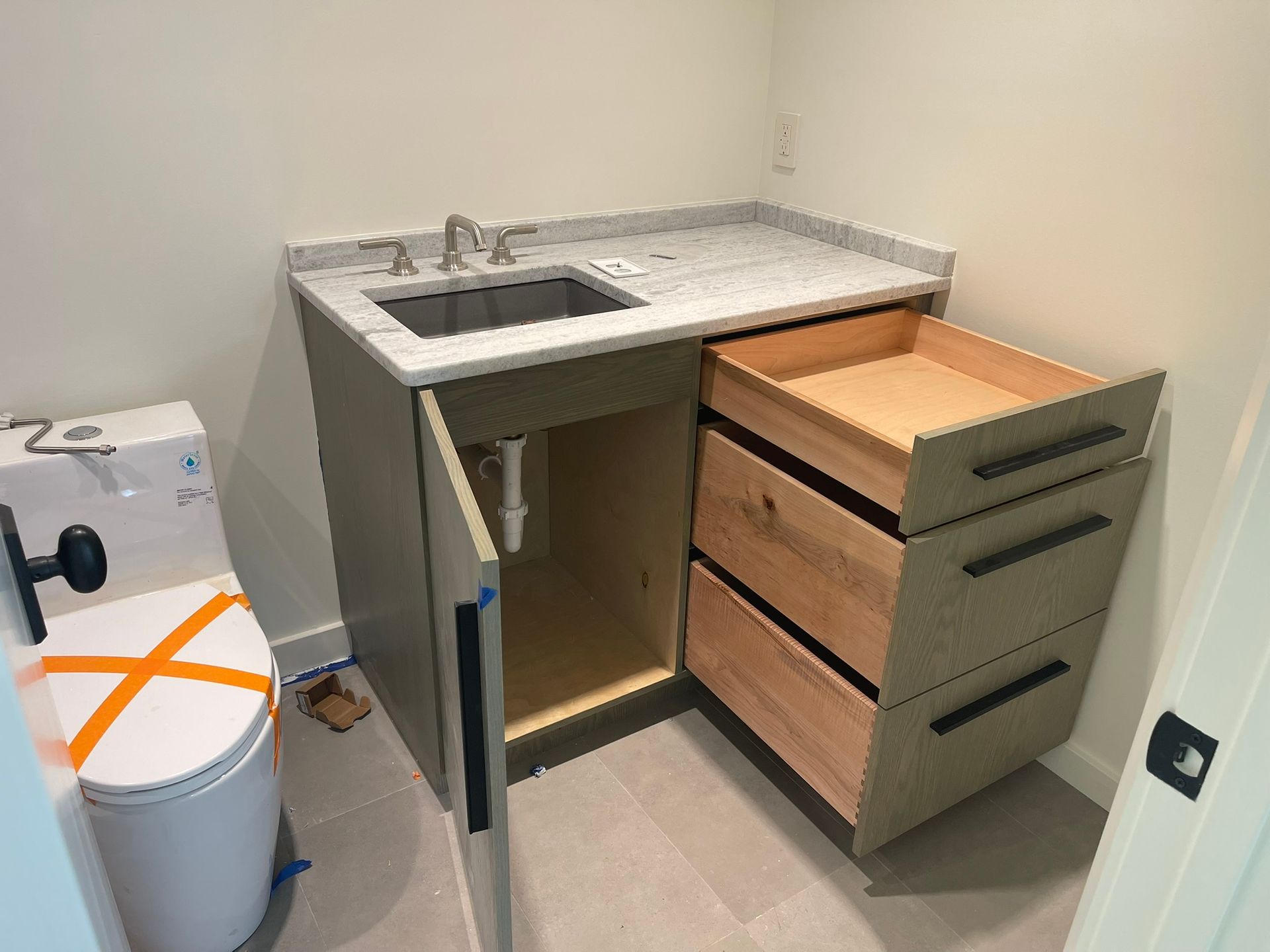 Bathroom with a sink, cabinet, open drawer, and toilet. Light-colored countertop, gray cabinet, and white walls.