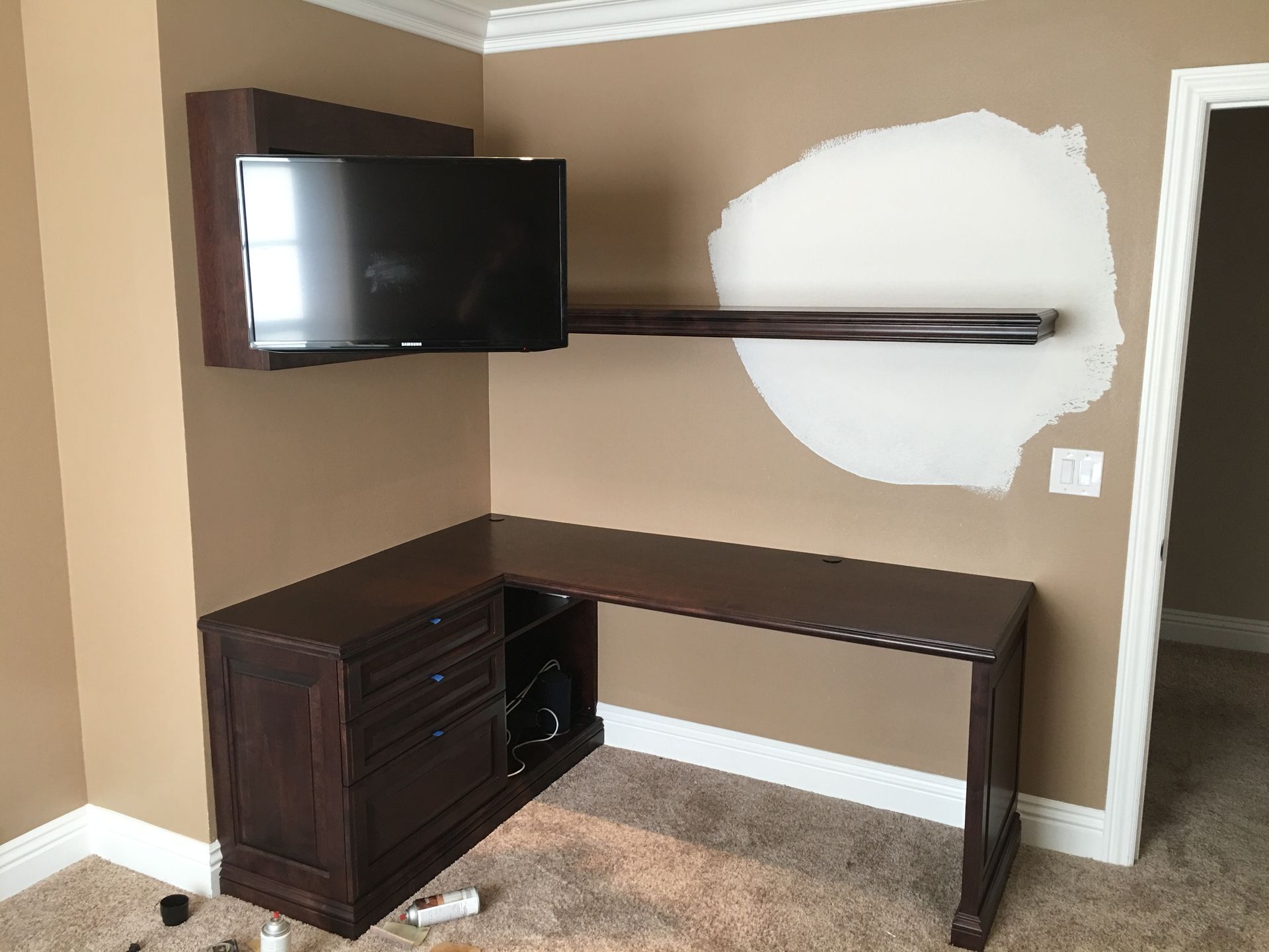 Dark wood desk with built-in drawers, mounted TV, and unfinished wall patch.