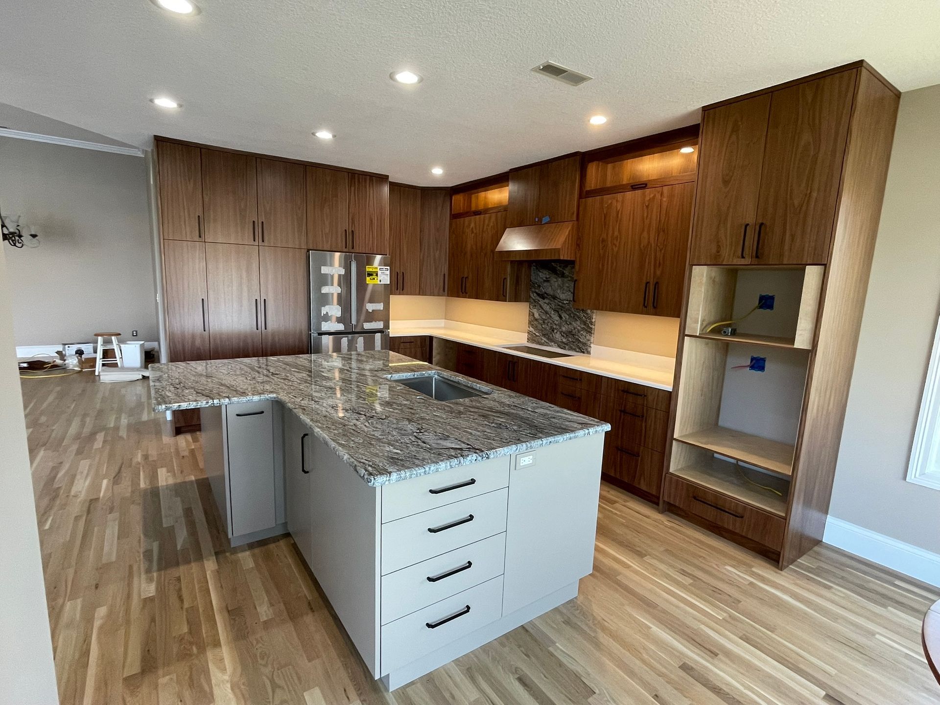 Kitchen with wood cabinets, gray island with granite countertop, stainless steel appliances, and wood flooring.