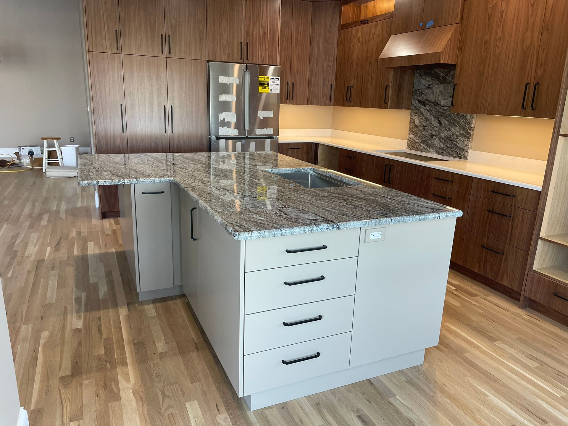 Modern kitchen with light island, dark wood cabinets, granite countertops, and stainless steel refrigerator.