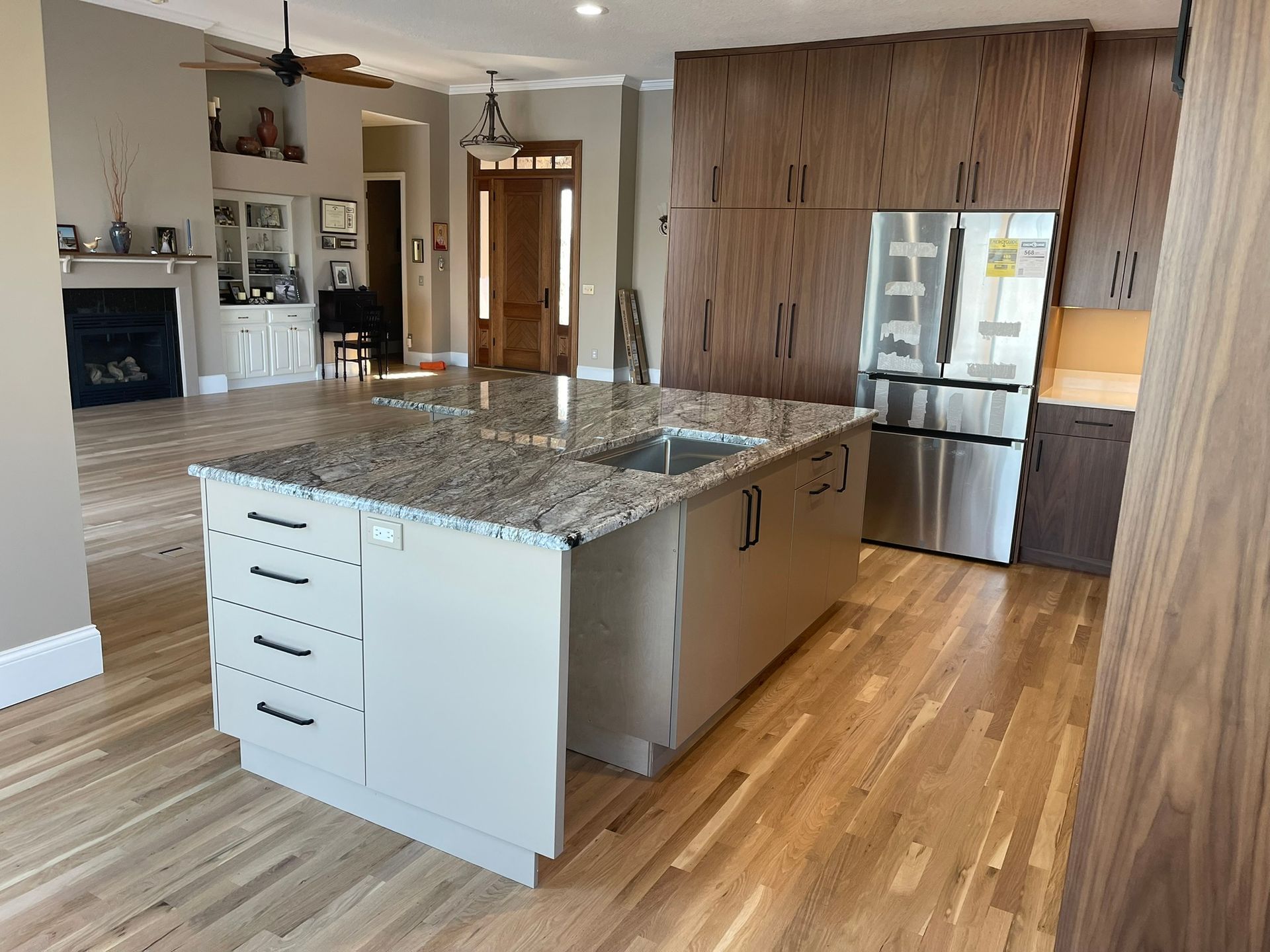 Kitchen with island, stainless steel refrigerator, and wood cabinets. Light wood flooring.