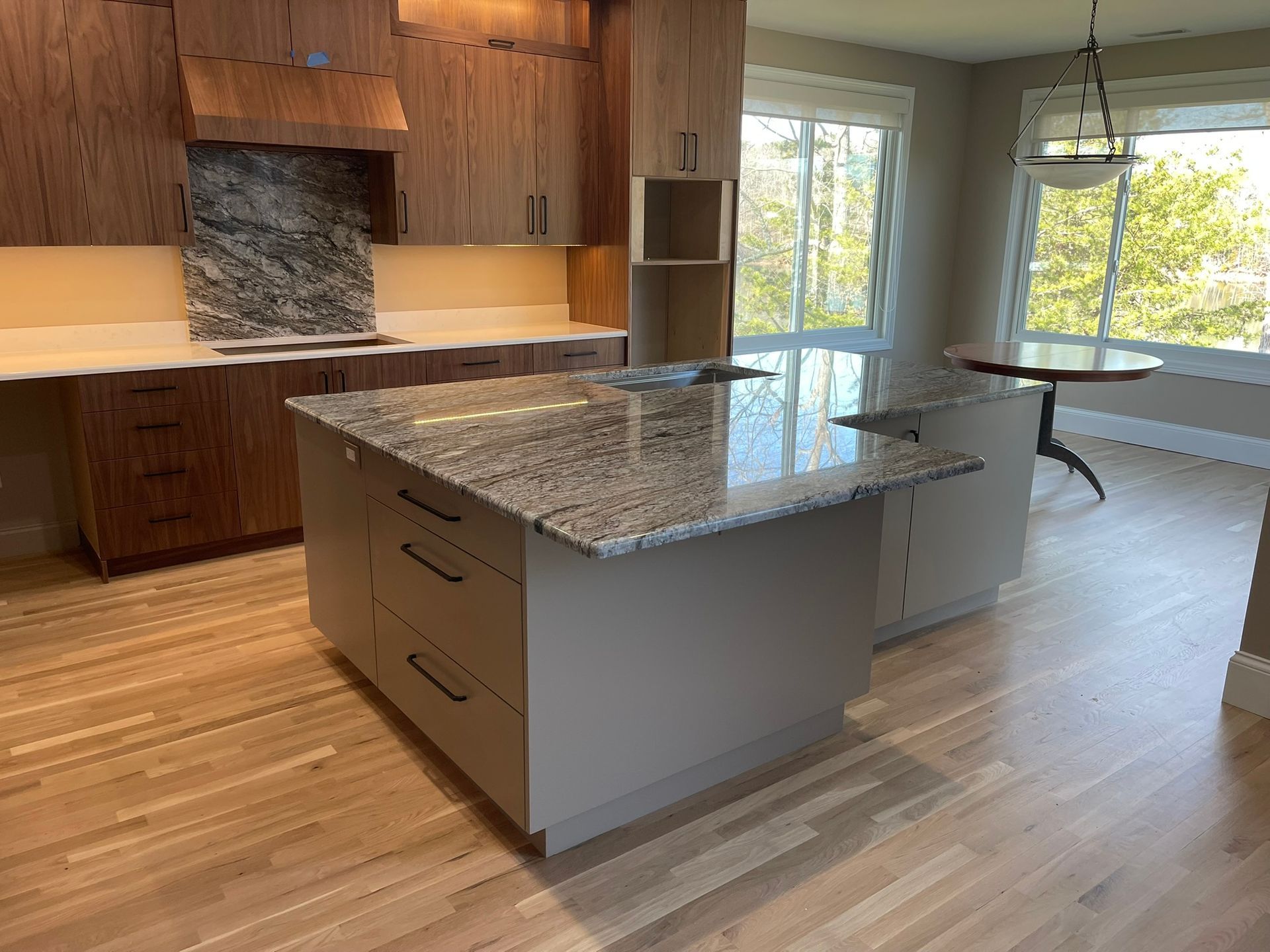 Modern kitchen with light wood cabinets, grey island, granite countertops, and hardwood floors.