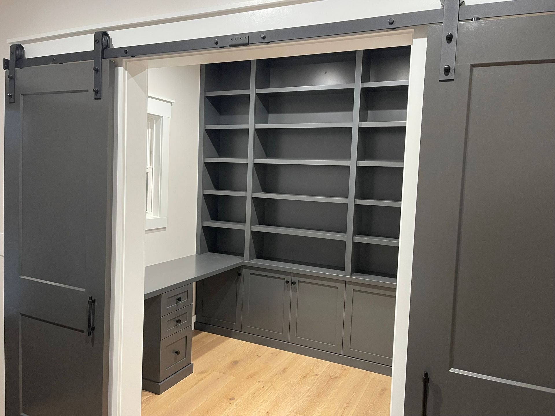 Gray home office with built-in bookshelves, desk, and sliding barn doors.
