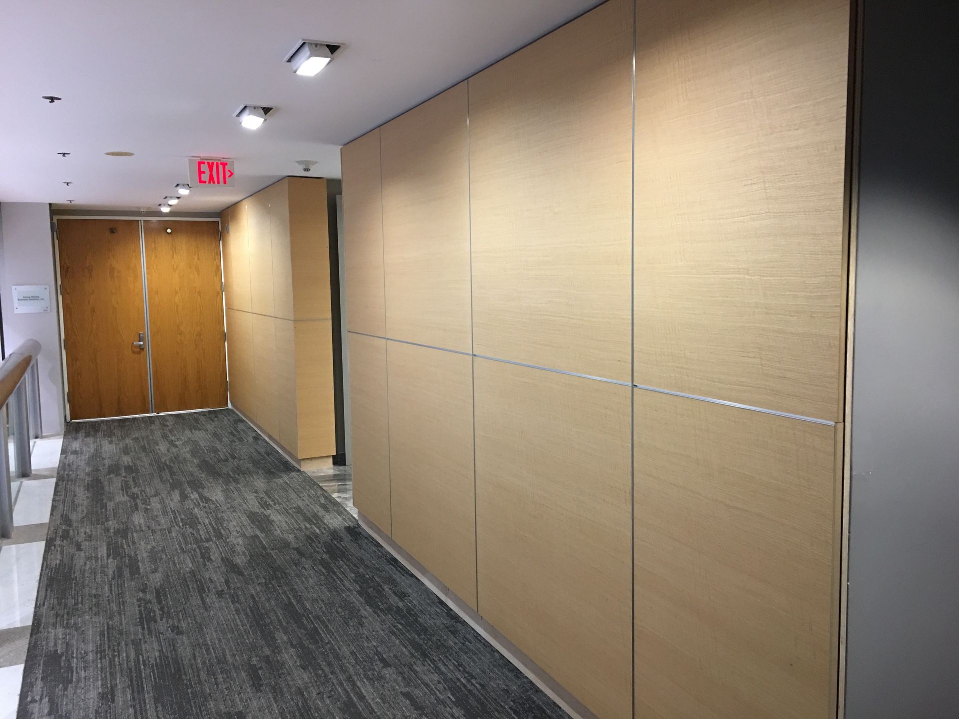 Hallway with wood panel wall, carpeted floor, and exit sign.