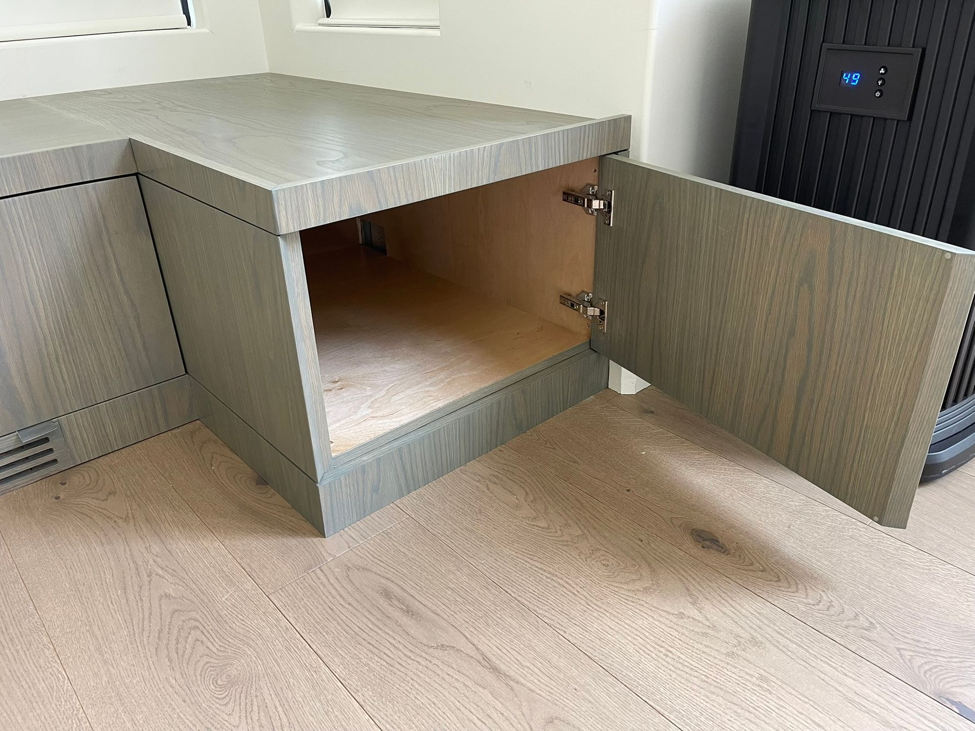 Gray cabinet with an open door, revealing an empty interior, on a light wood floor.