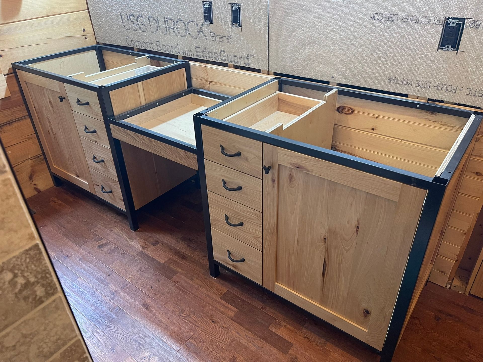 Bathroom vanity cabinets under construction, wood with dark metal frame accents.