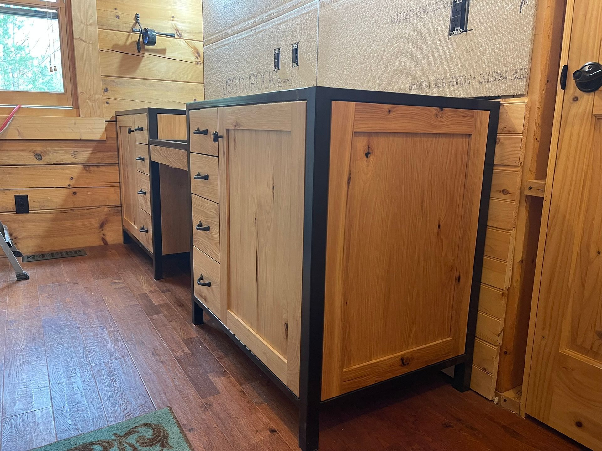 Two wooden bathroom vanities with black metal frames in a log cabin setting.
