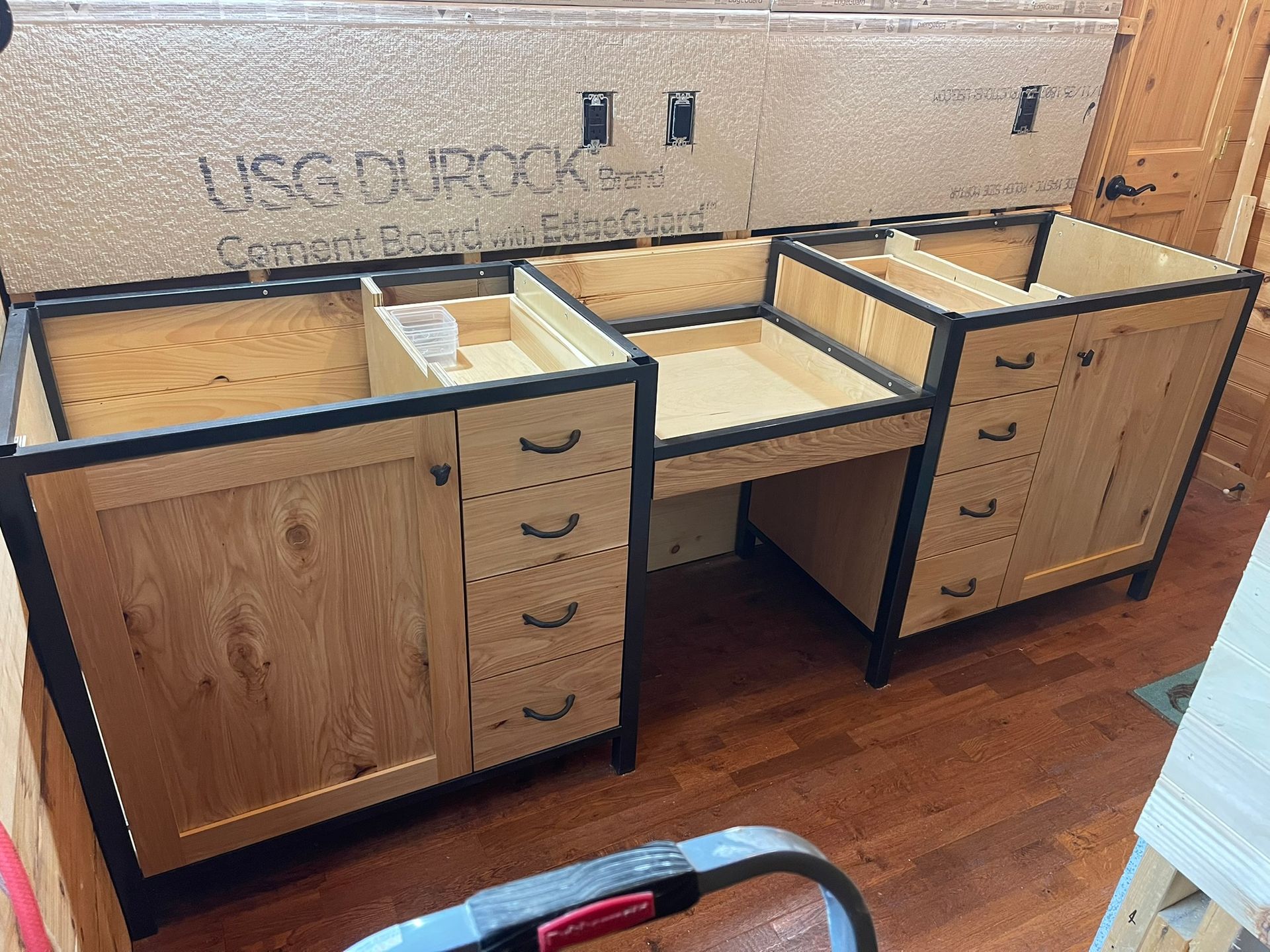 Wooden bathroom vanity under construction with black trim and drawers.