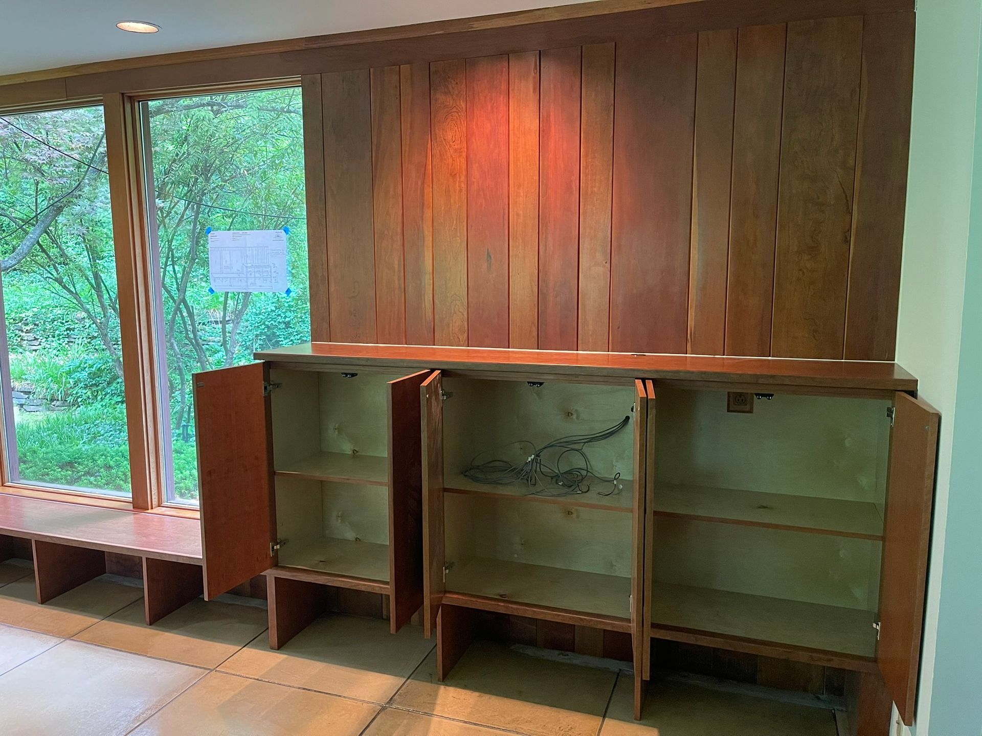 Wooden cabinets with open doors, against a wooden wall and window overlooking greenery.