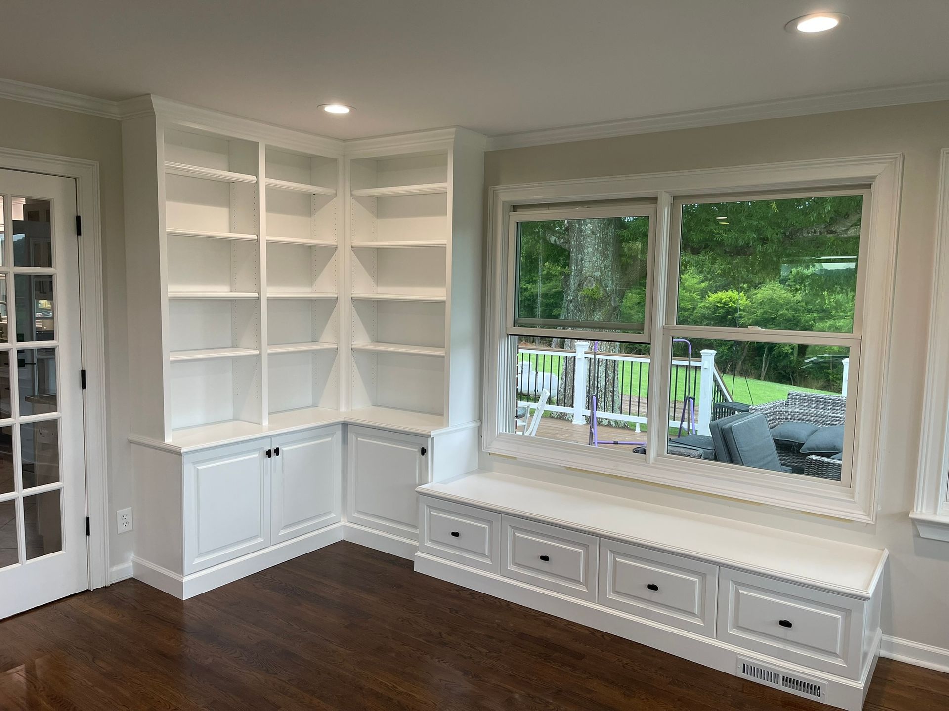 White built-in bookshelves and window seat with drawers in a room with a dark wood floor.