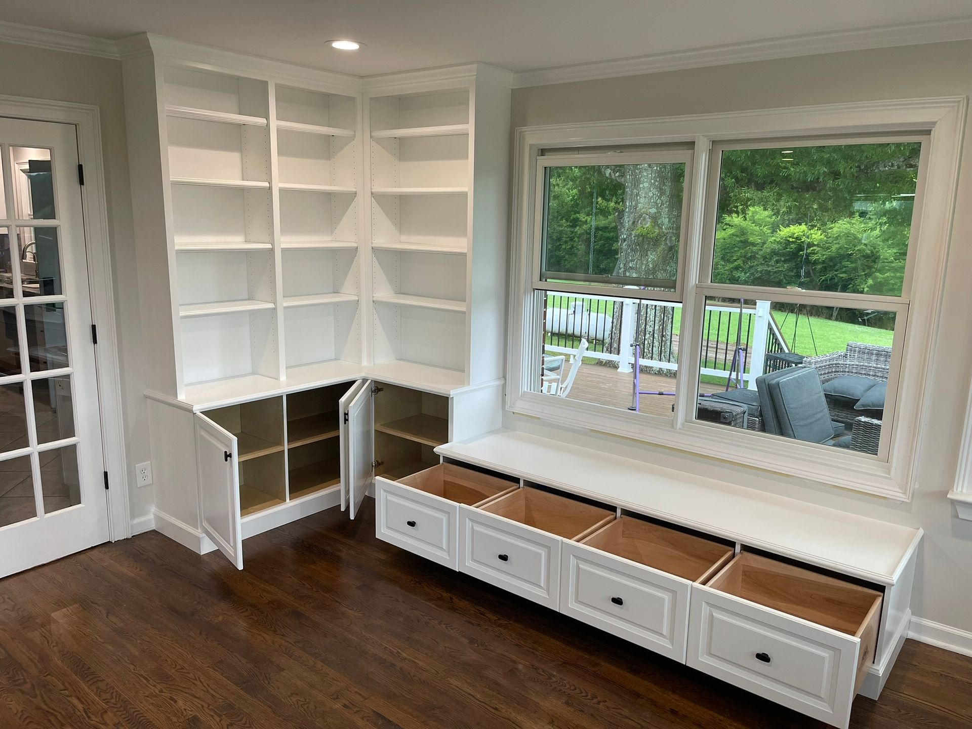 Built-in white bookshelves and storage bench by a window, with open drawers and cabinets.