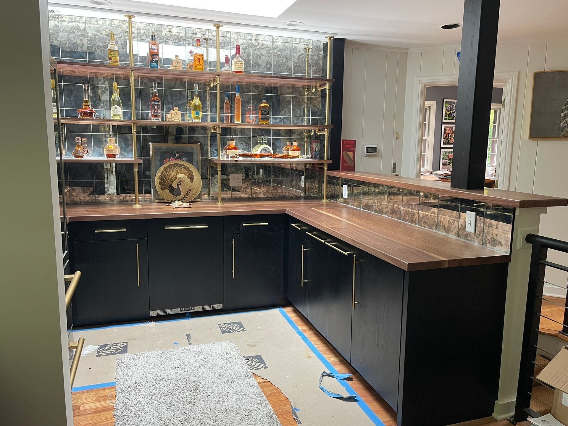 Home bar with black cabinets, brass shelving, and liquor bottles on display.