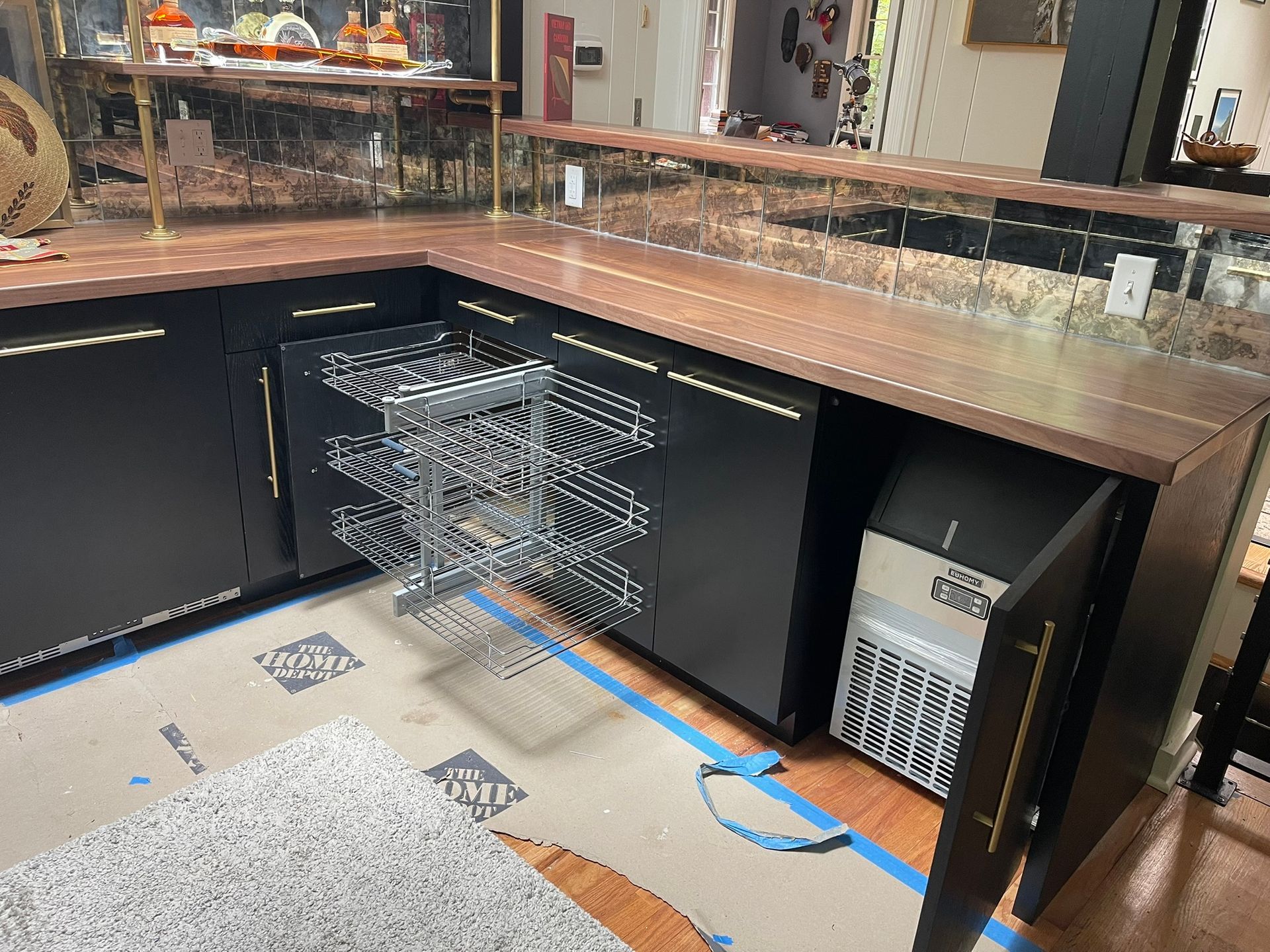 Black cabinets with copper countertop and pull-out wire shelving unit and ice maker.