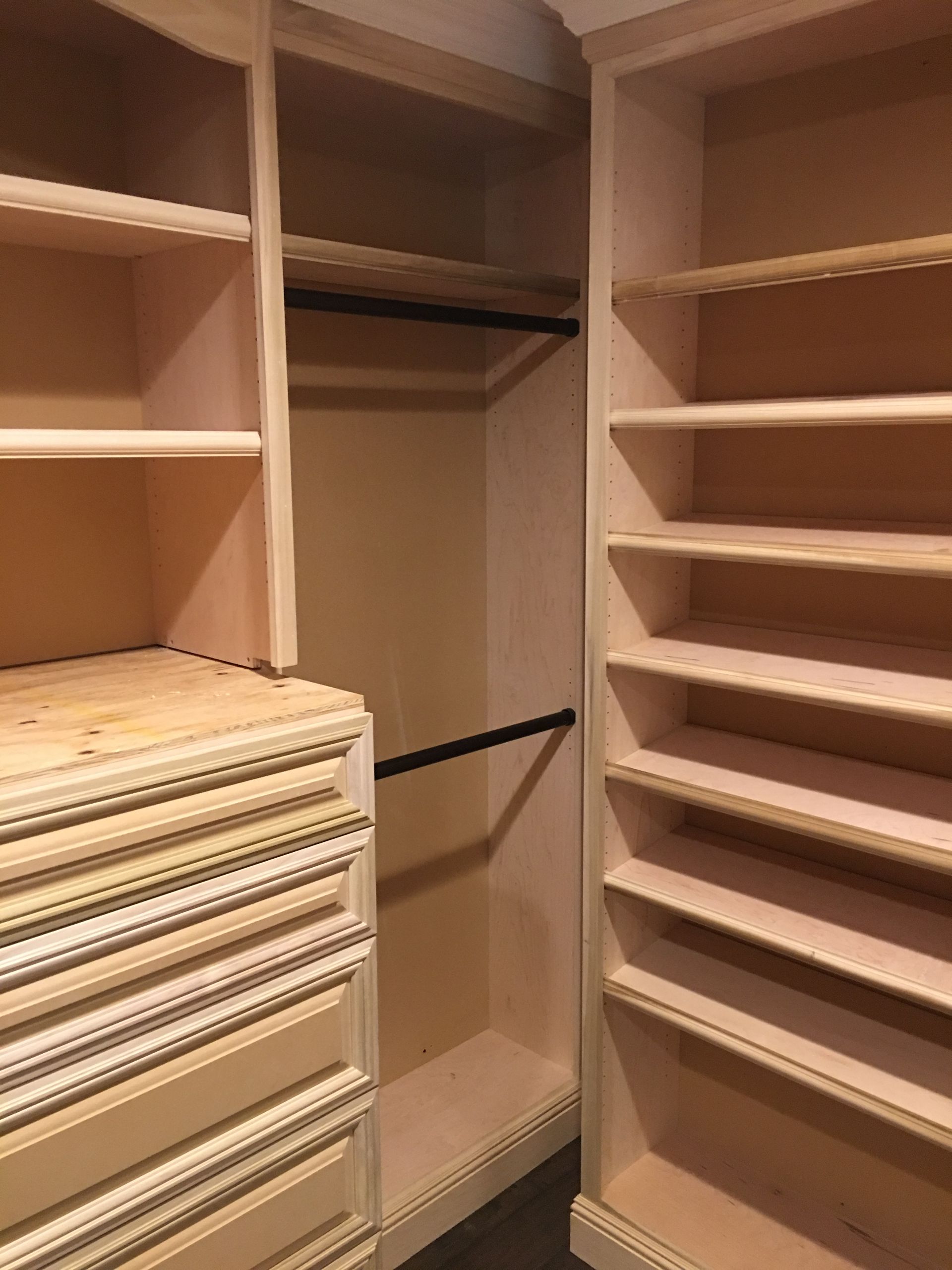 Walk-in closet with shelves and drawers. Two dark rods for hanging clothes. Light wood construction.