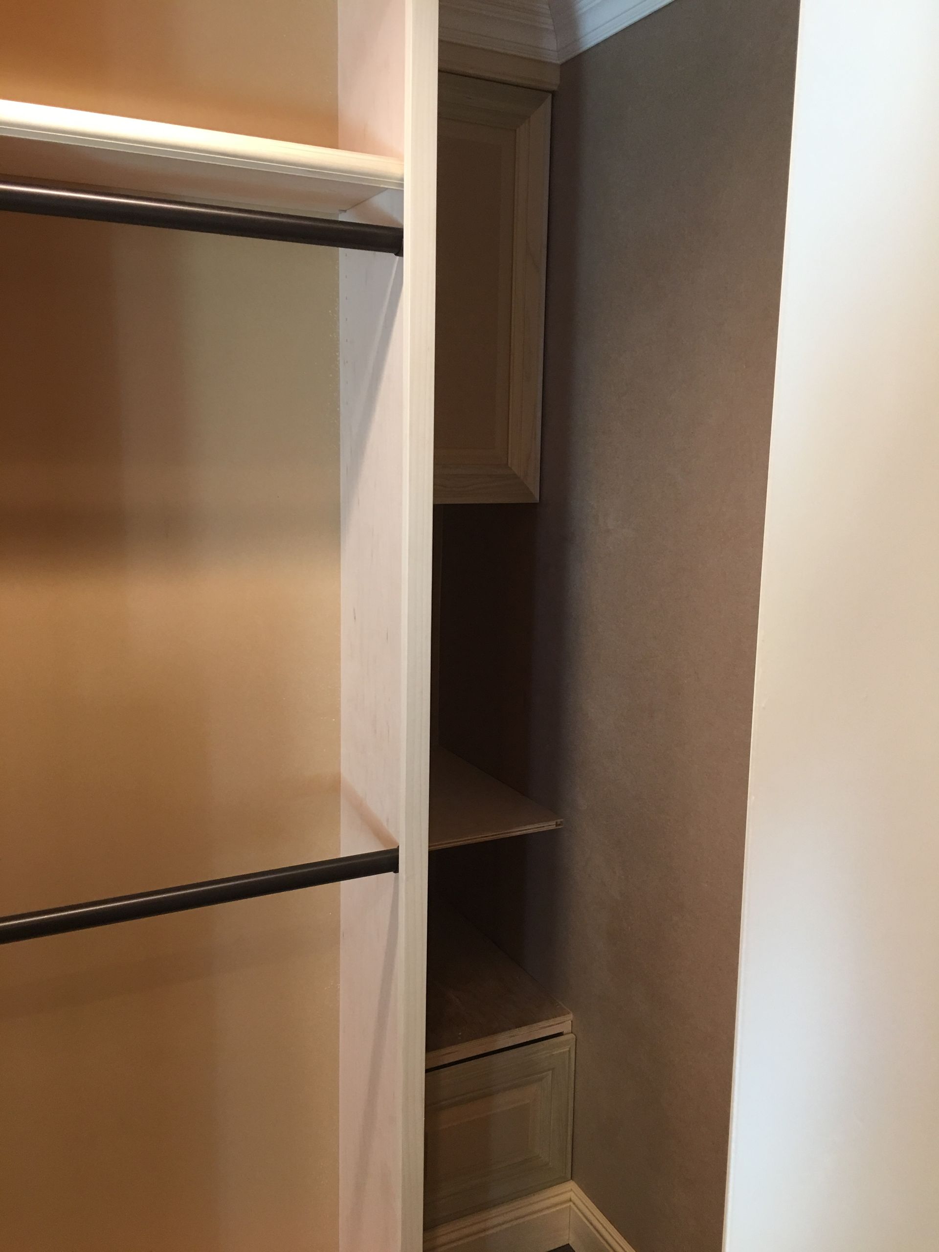 Built-in closet with hanging rods, shelves, and a small cabinet. Beige walls and trim.