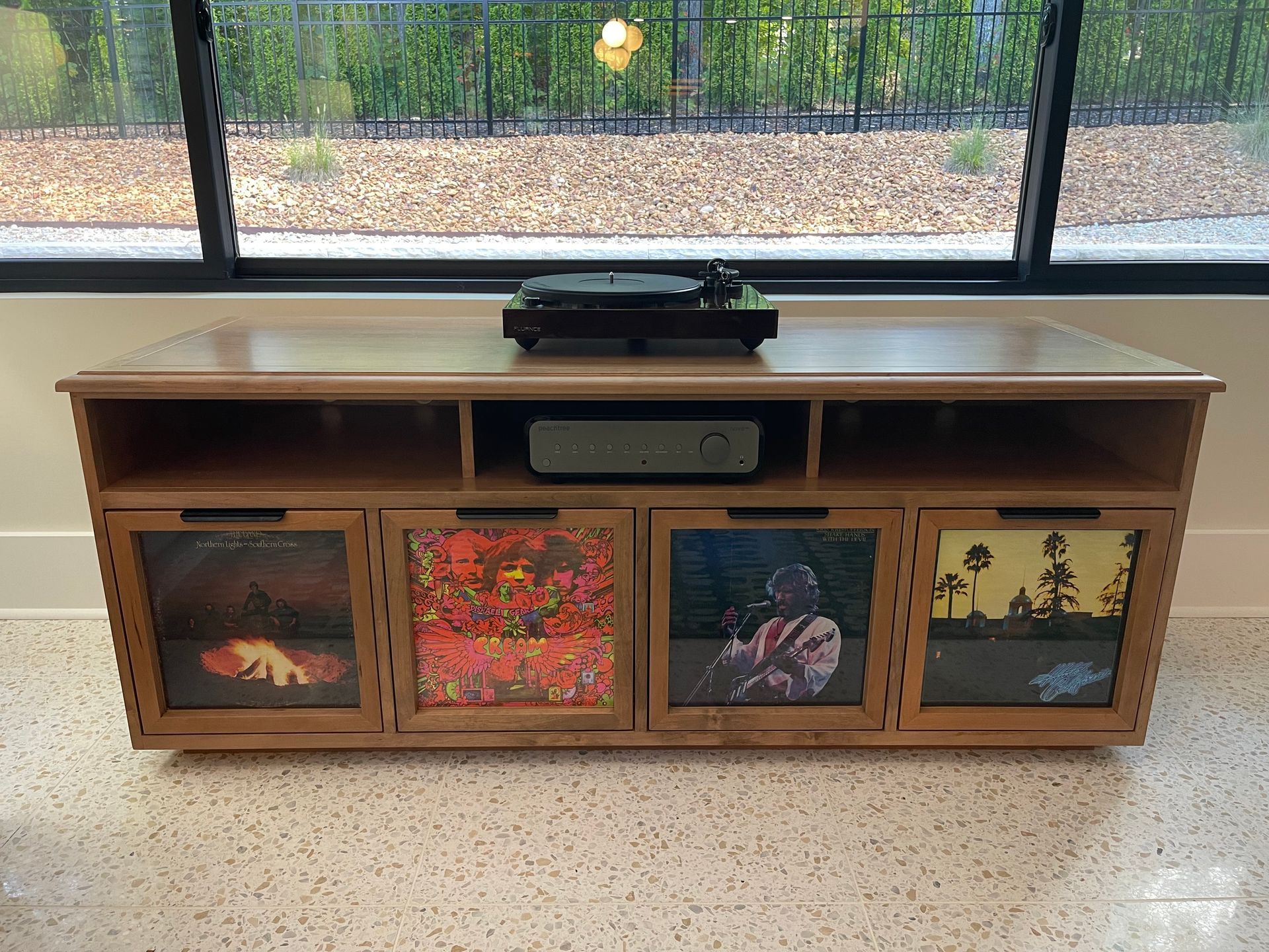 A wooden record cabinet with a turntable, amplifier, and vinyl records displayed behind glass doors.