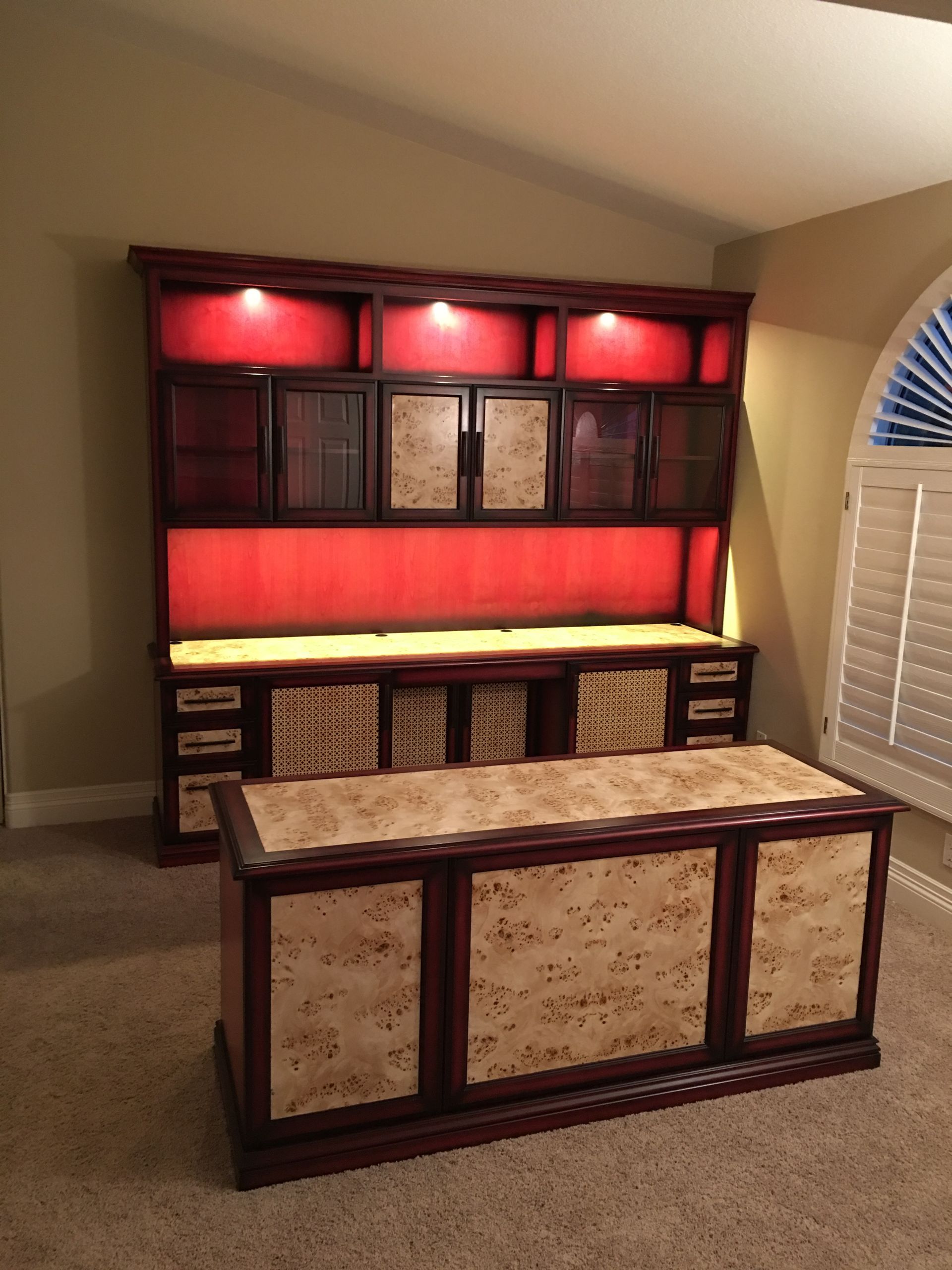 Custom built-in desk and cabinet with red backlighting and light-colored wood accents in a room.